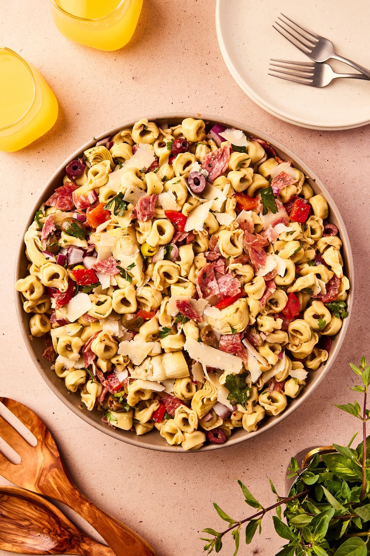 Large bowl filled with tortellini pasta salad filled with lots of olives, Parmesan cheese, artichoke hearts, and bell pepper on taupe surface.