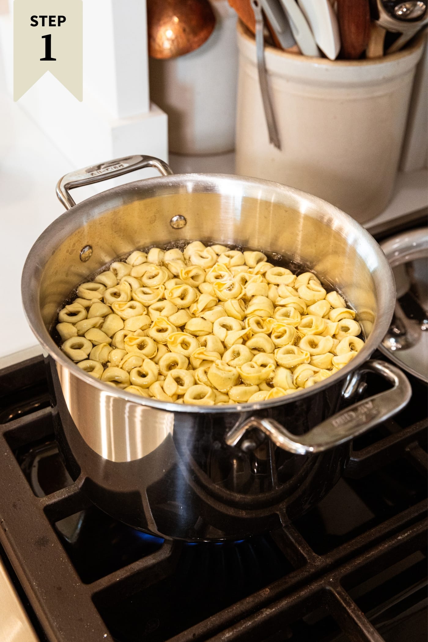 Large metal stockpot sitting on heat on stovetop filled with uncooked stuffed tortellini pasta.