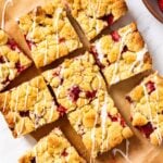 White marble surface with strawberry crumb bars cut into pieces and drizzled with white glaze over the top.