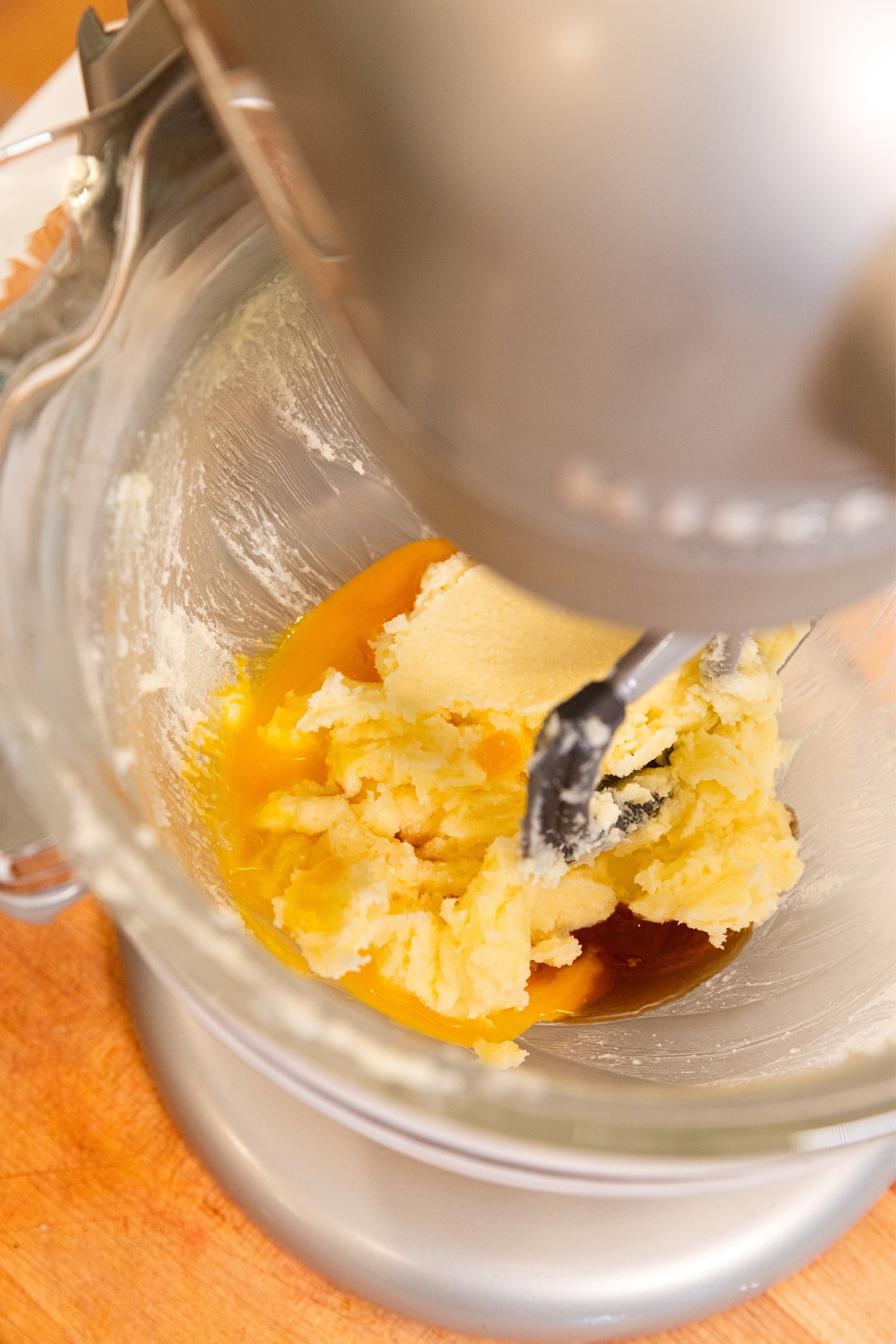 Stand mixer with glass bowl filled with butter and sugar, eggs, and vanilla extract.