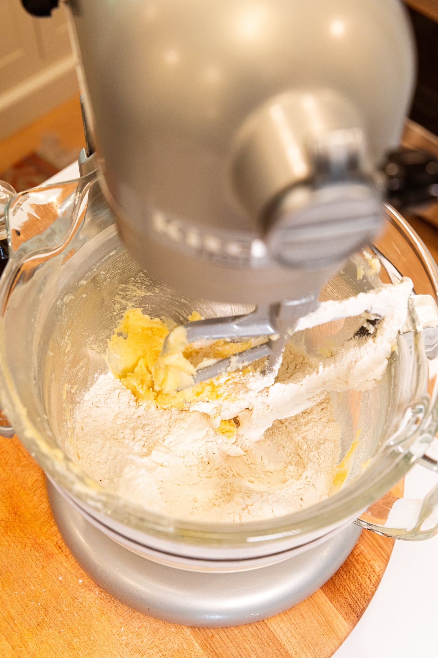 Stand mixer will creamed butter and sugar mixture with flour sprinkled on top.