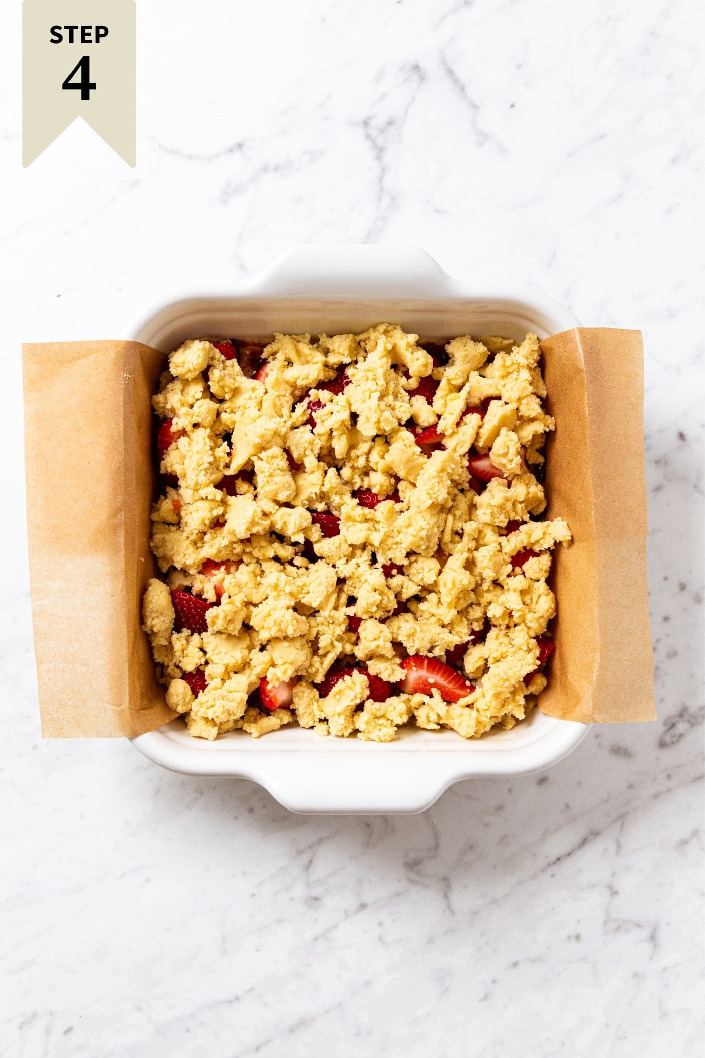 Square baking dish lined with parchment paper with unbaked strawberry crumb bars right before going into the oven.