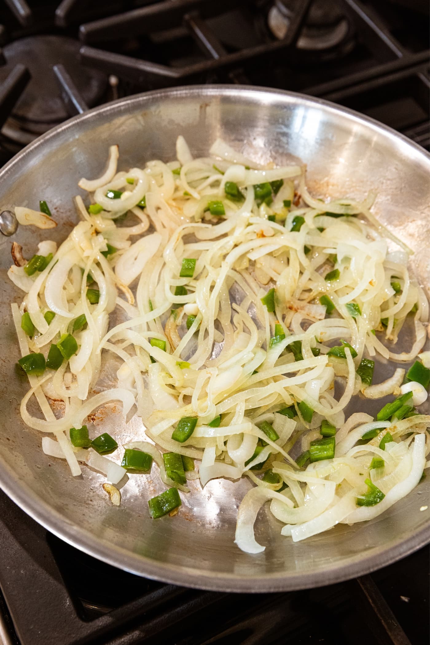 Metal skillet on stove with sliced onions and pieces of jalapeño after getting some browning on them.