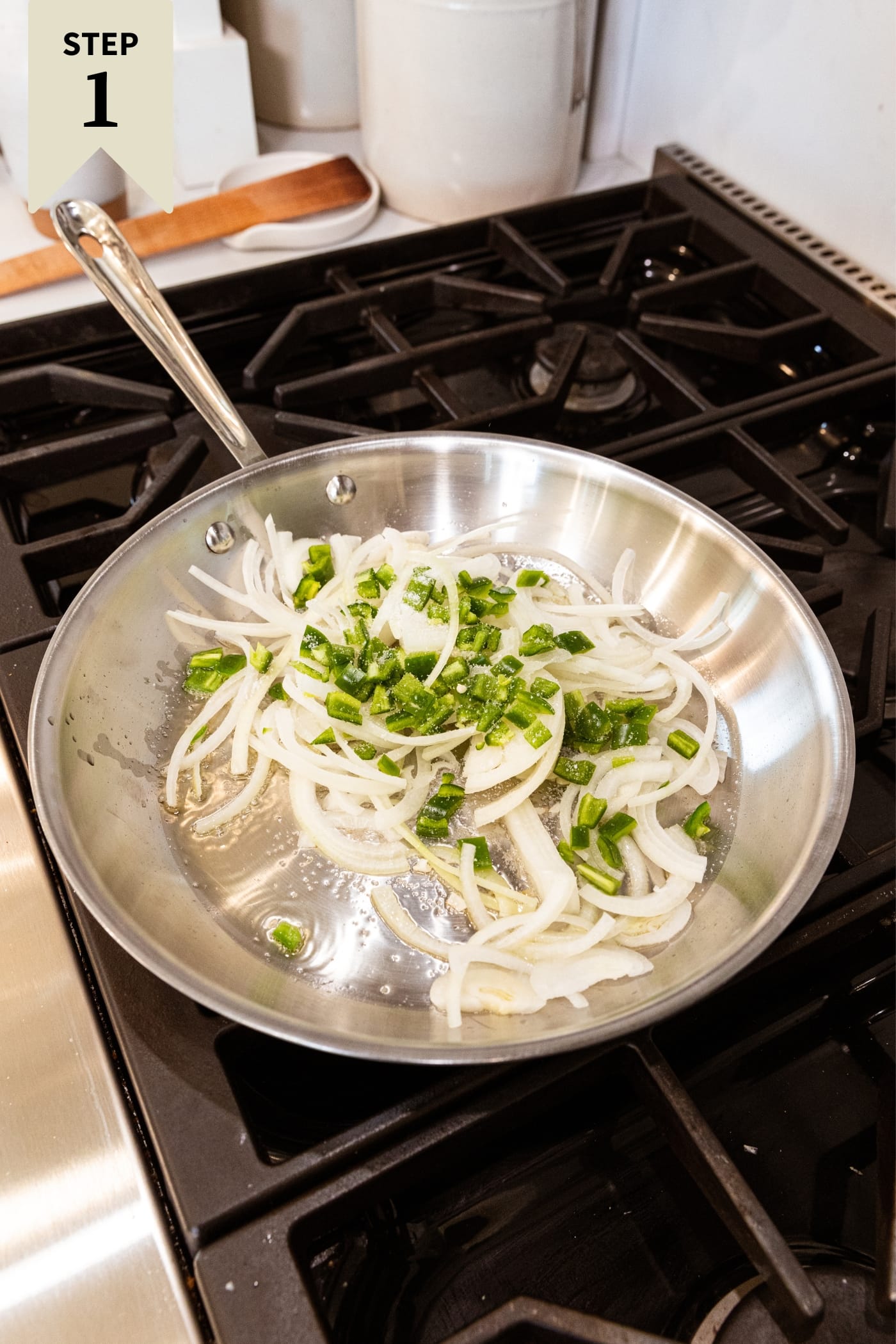 Metal skillet sitting on stovetop filled with sliced onion and diced jalapeño before being browned.
