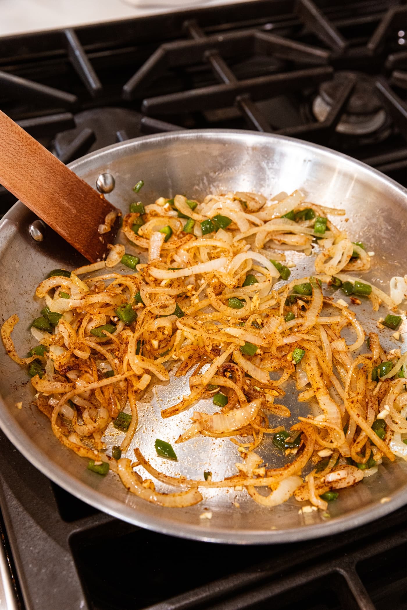 Metal skillet with brown slices of onion and diced jalapeño after being mixed with brown spices.