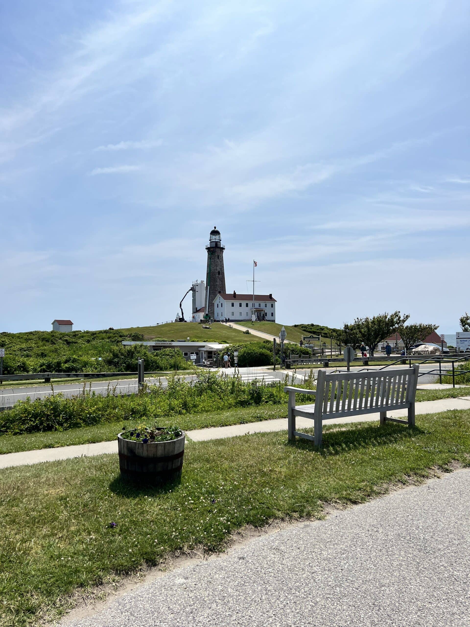 Montauk lighthouse at the peak of the island with park bench in the foreground with path leading up to the lighthouse.