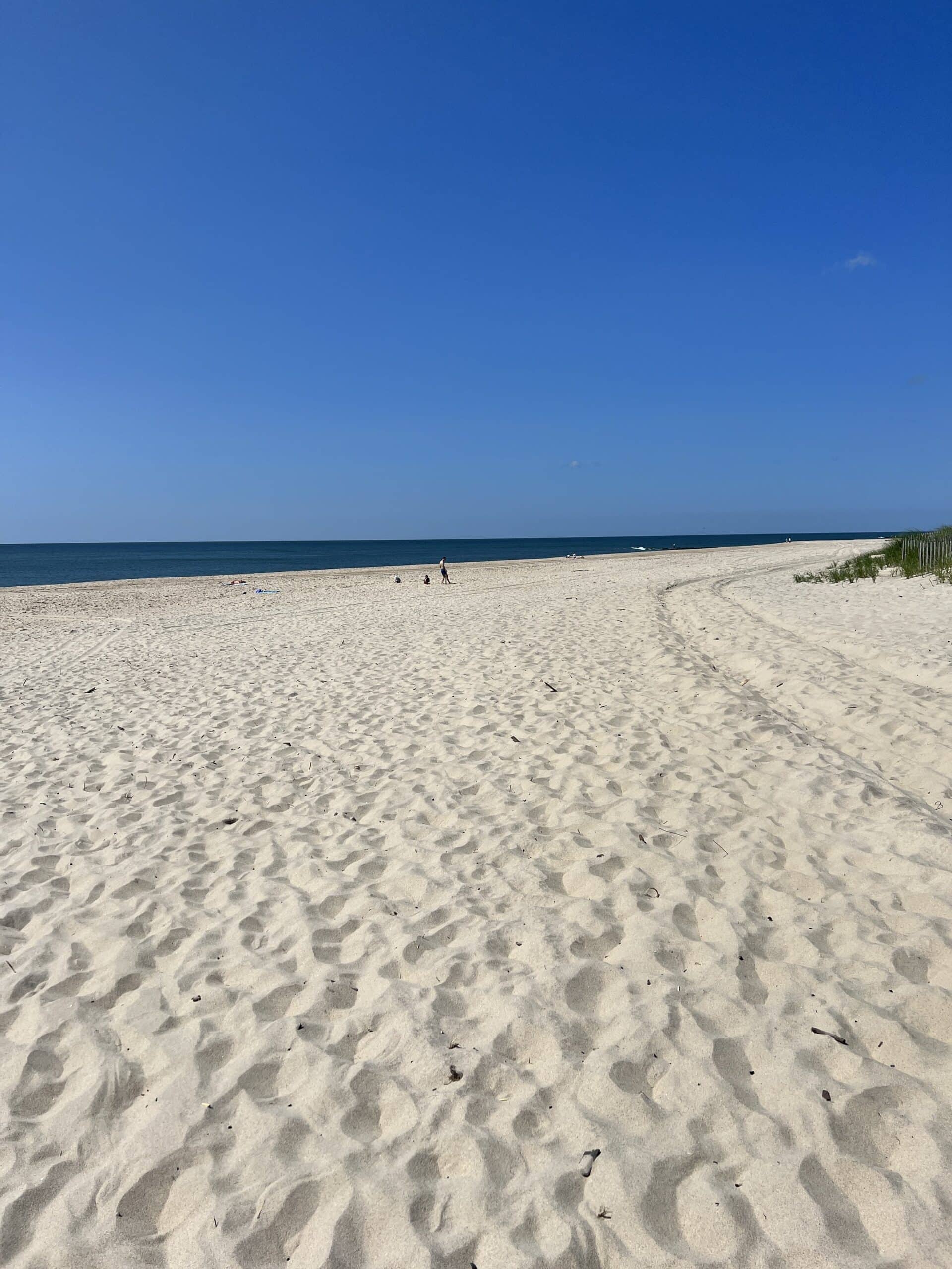 Sand along beach with bright blue sky with footprints all over the surface of the sand.
