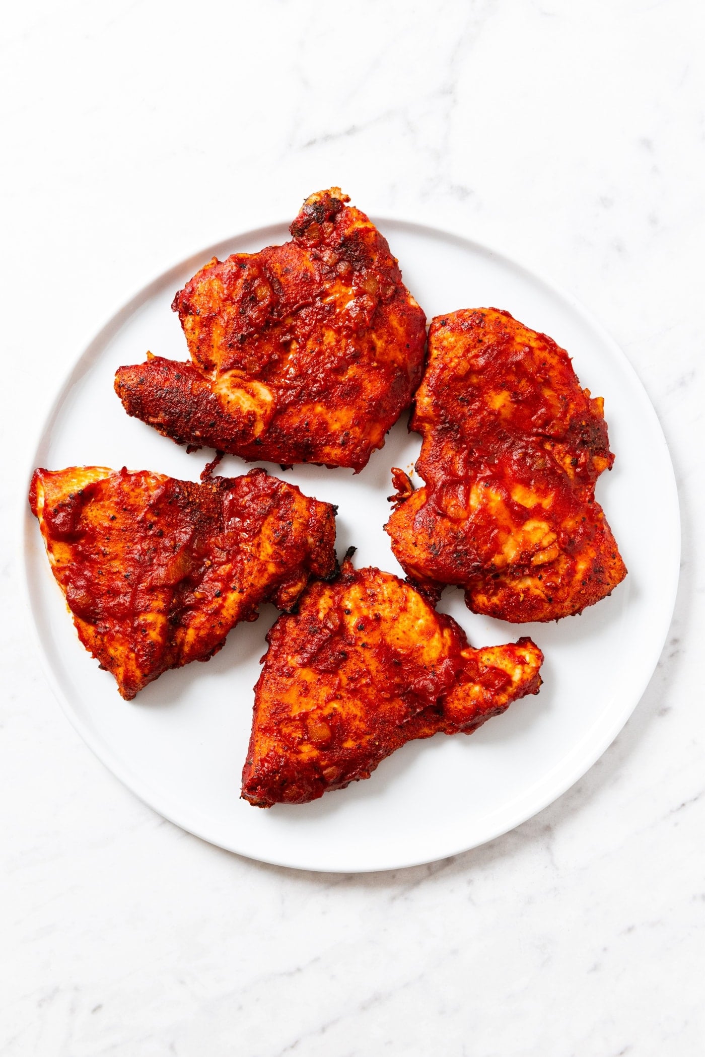 Round white plate sitting on marble surface with four pieces of grilled barbecue chicken.