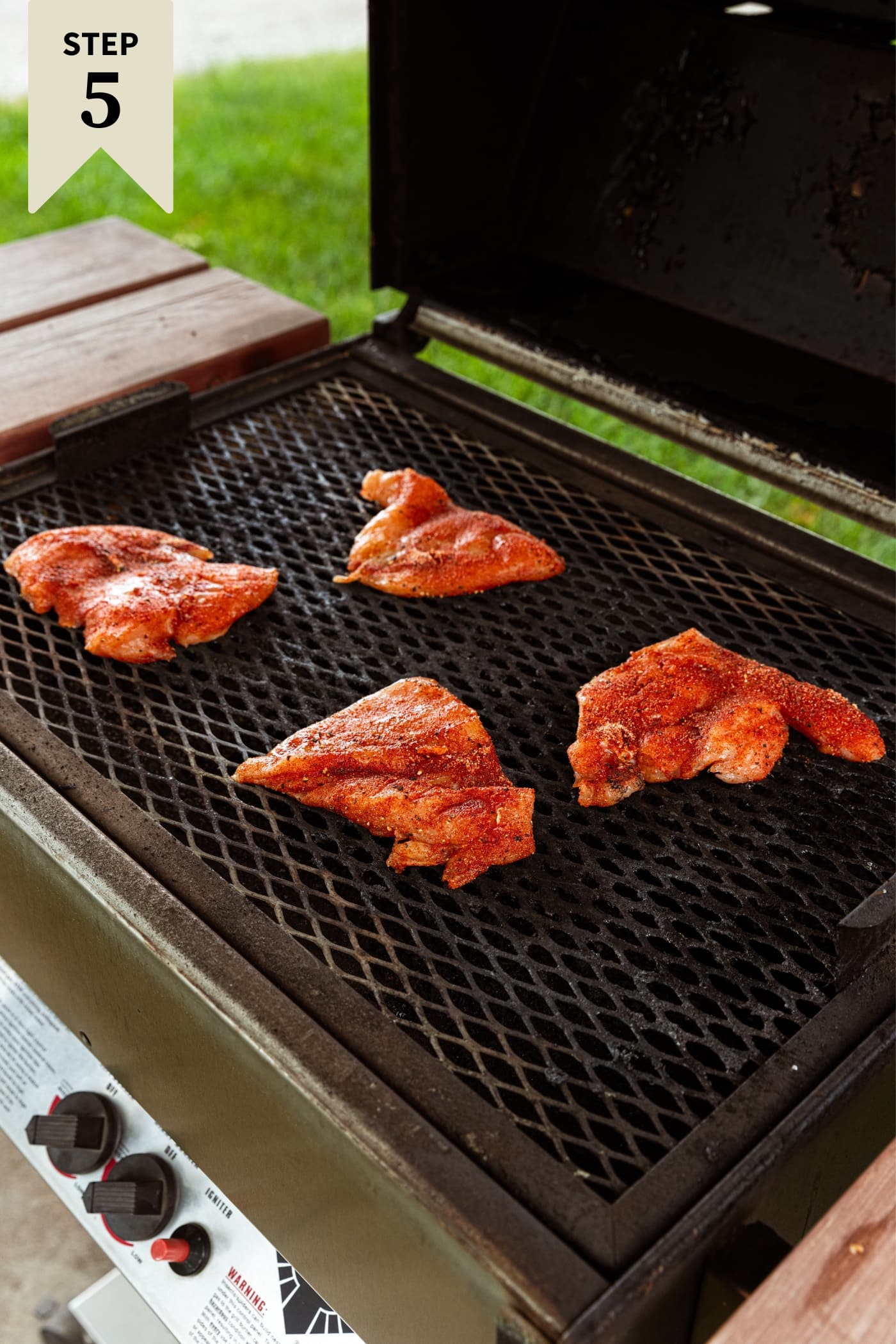 Raw pieces of chicken breast sitting on grates of grill right before being browned.