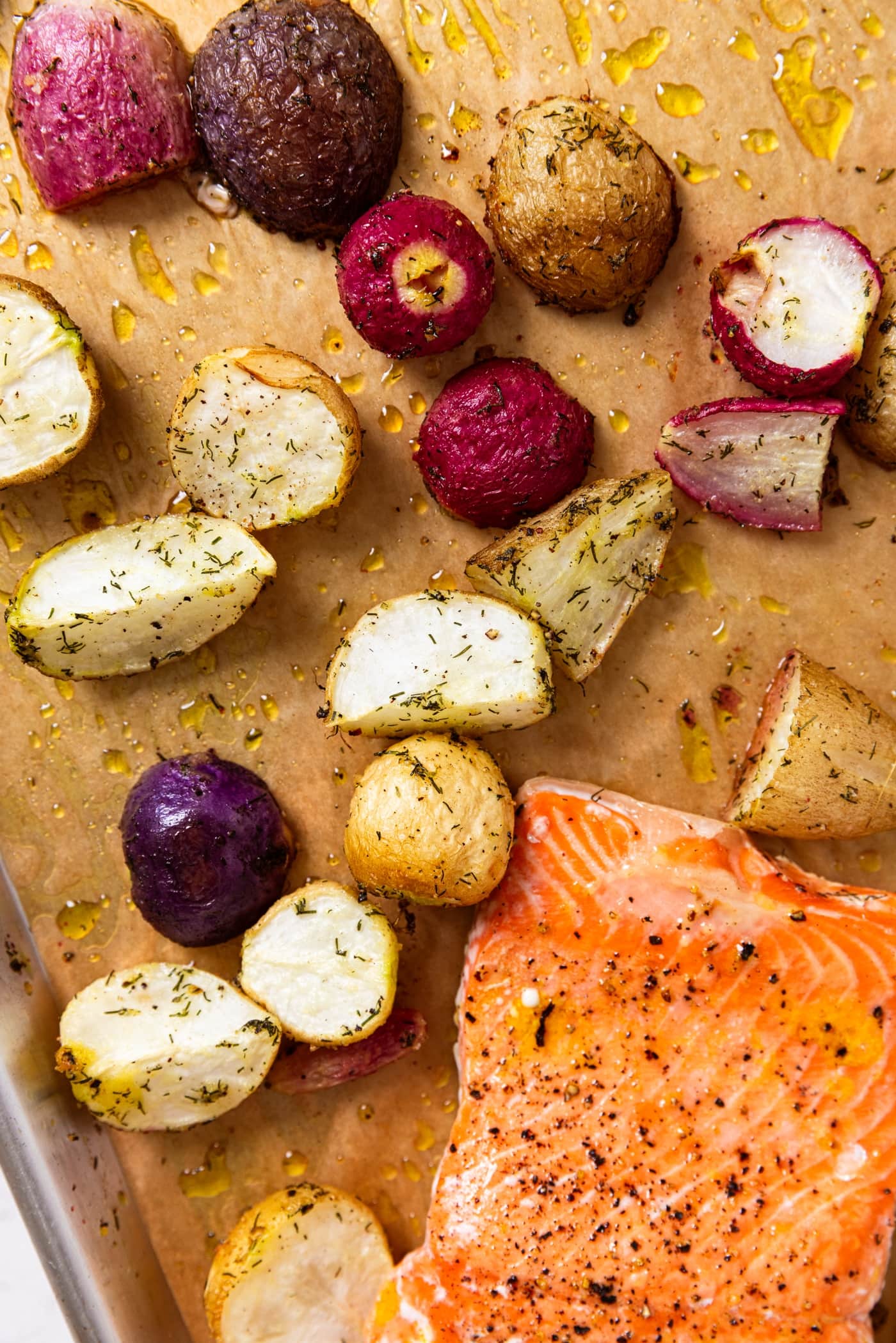 Baking sheet lined with parchment with salmon filets and sliced radishes sprinkled with dried herbs right after coming out of the oven.