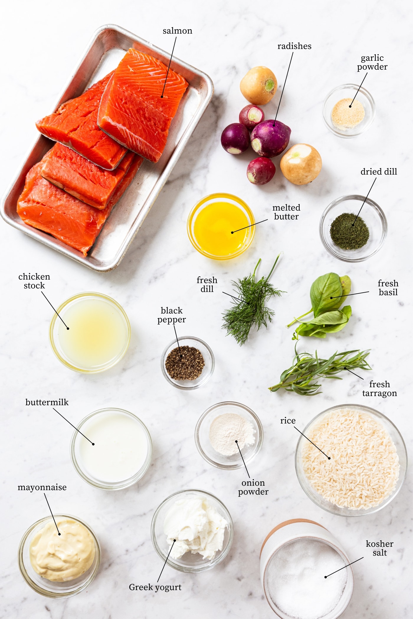 White marble surface filled with all ingredients needed to prepare roasted salmon including raw salmon, melted butter, spices, fresh herbs, rice, yogurt, salt, and more.