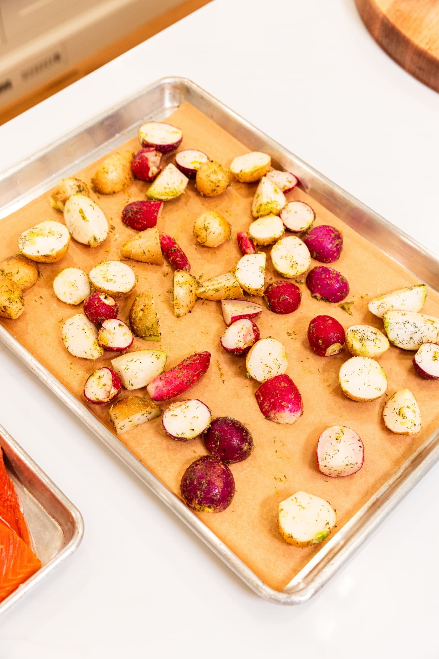 Sliced radishes sitting on parchment-lined baking sheet with dried herbs and melted butter all over the radishes sitting on white surface.