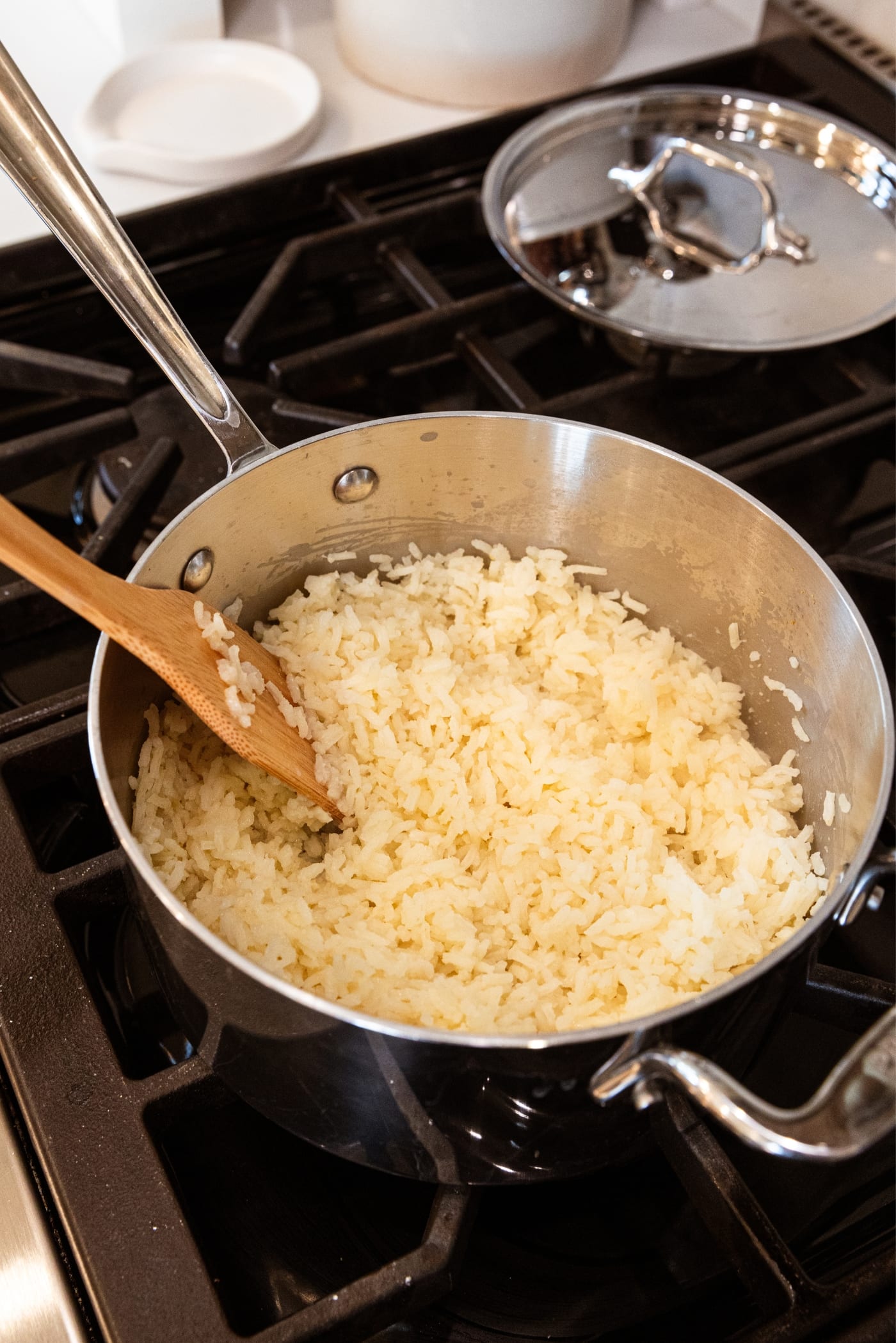 Small kettle on stovetop with cooked rice with wooden spoon resting against the side of the kettle.
