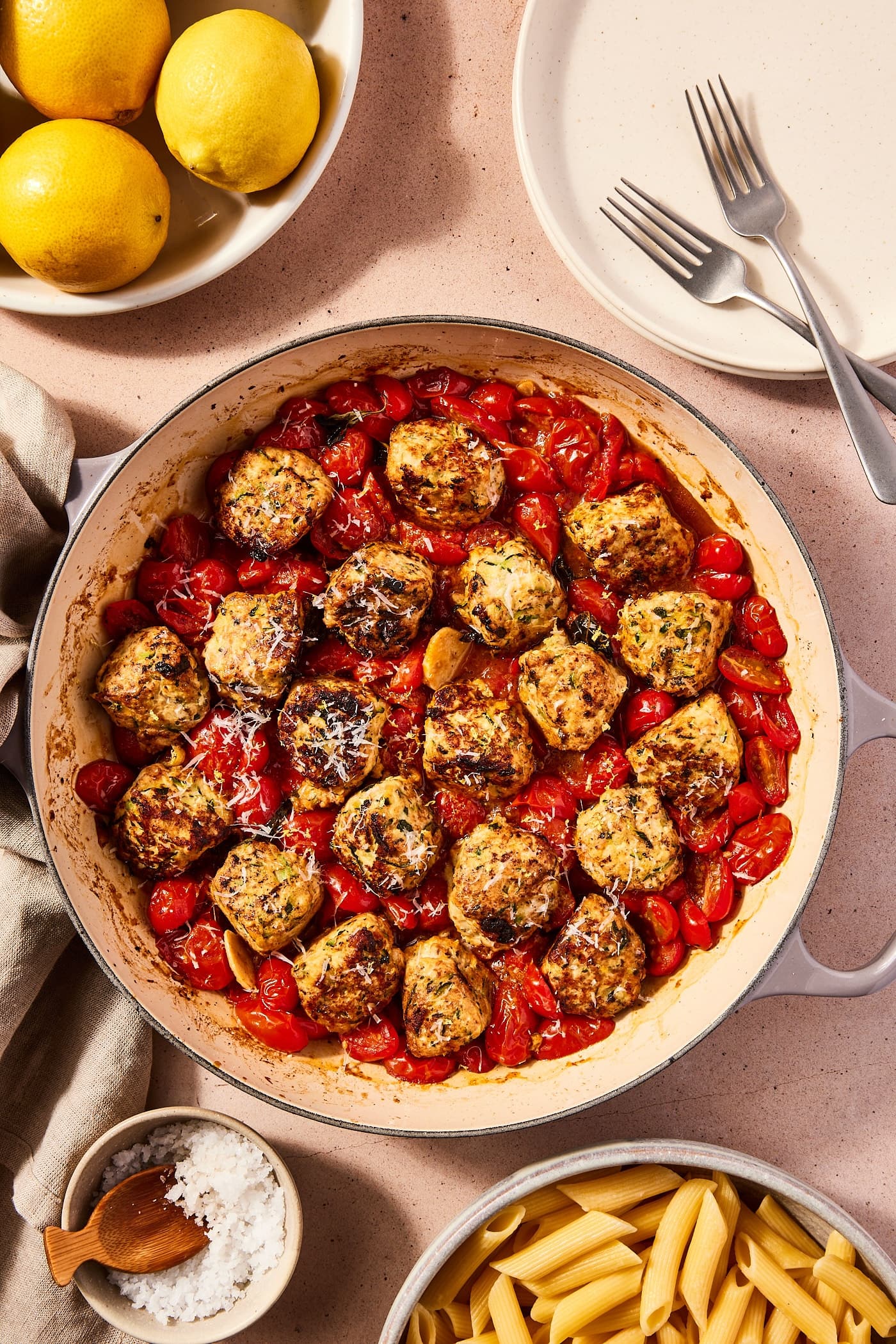 Large skillet filled with cooked chicken zucchini meatballs with tomato sauce all around after coming out of the oven with bowl of pasta and salt to the side.