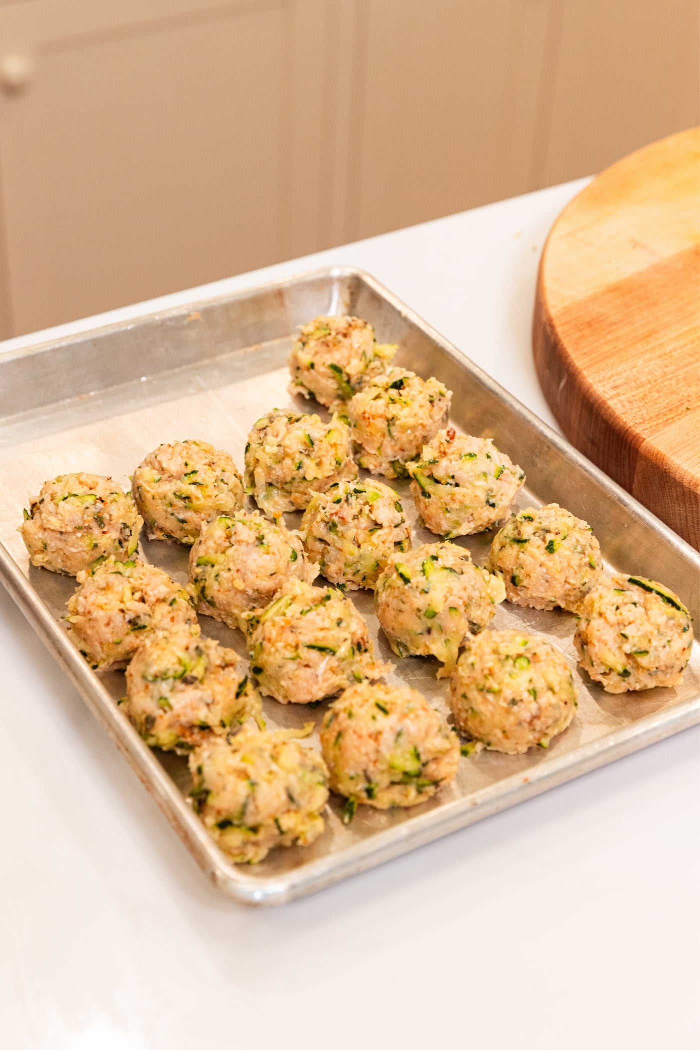 Baking sheet lined with round uncooked chicken zucchini meatballs before being cooked.