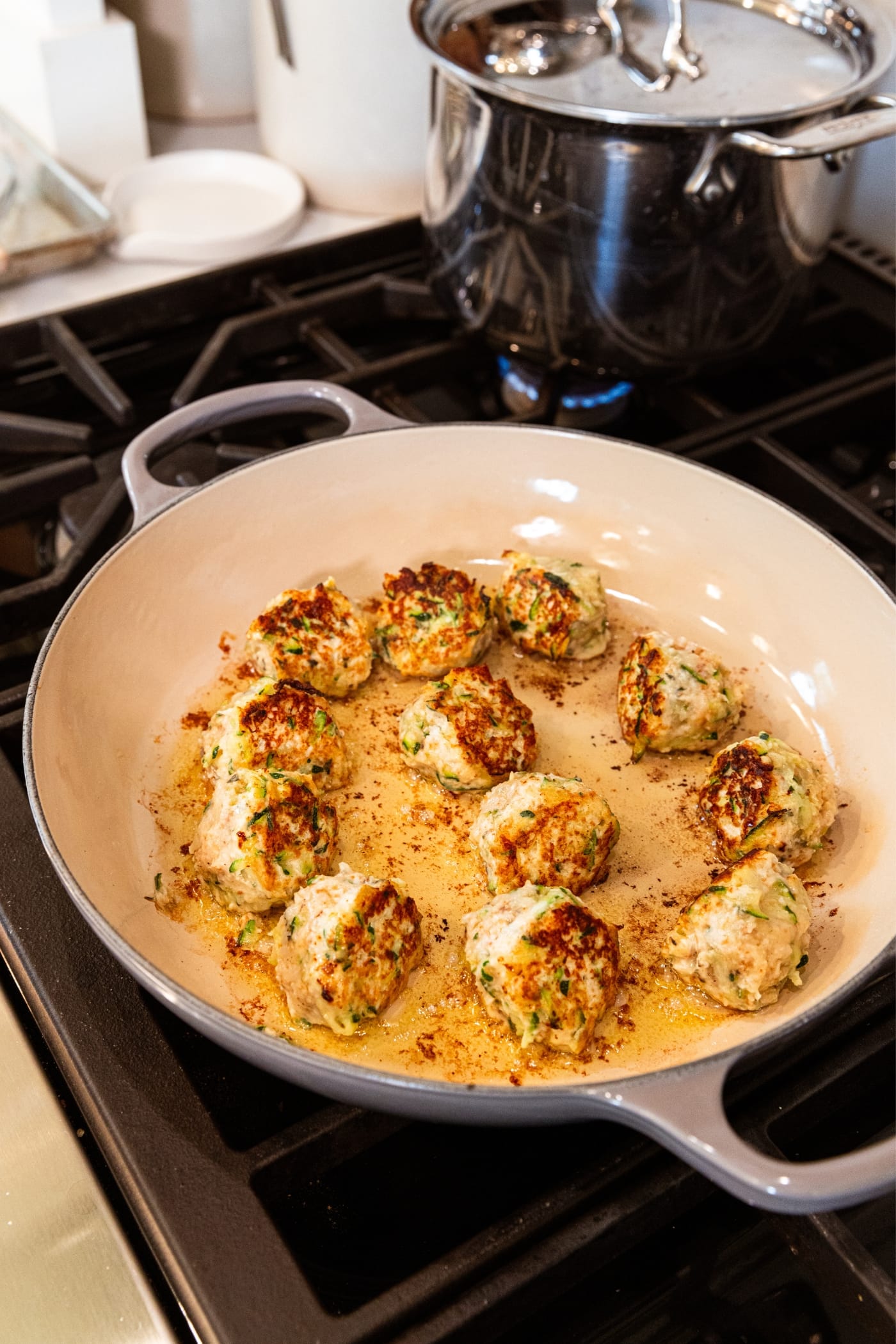 Large gray skillet on stovetop with browned chicken zucchini meatballs in a small amount of oil.