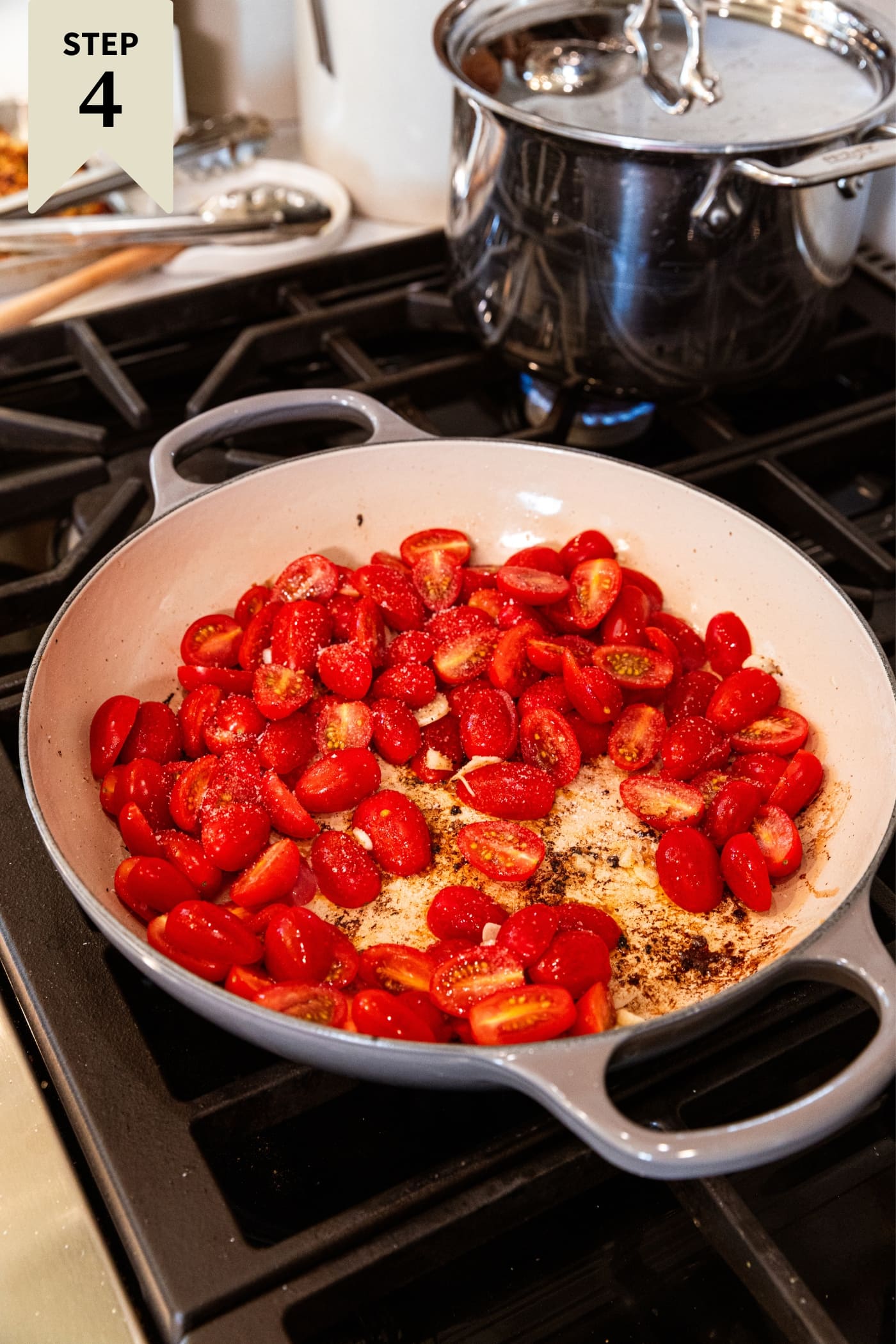 Round gray skillet sitting on the stovetop with sliced grape tomatoes before being cooked fully.