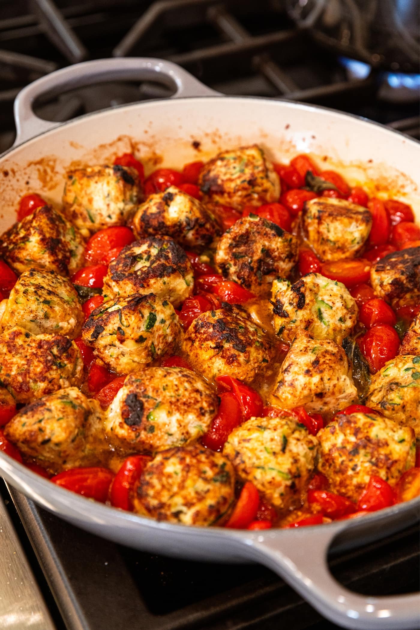 Round chicken meatballs sitting in tomato sauce in gray skillet on the stovetop.