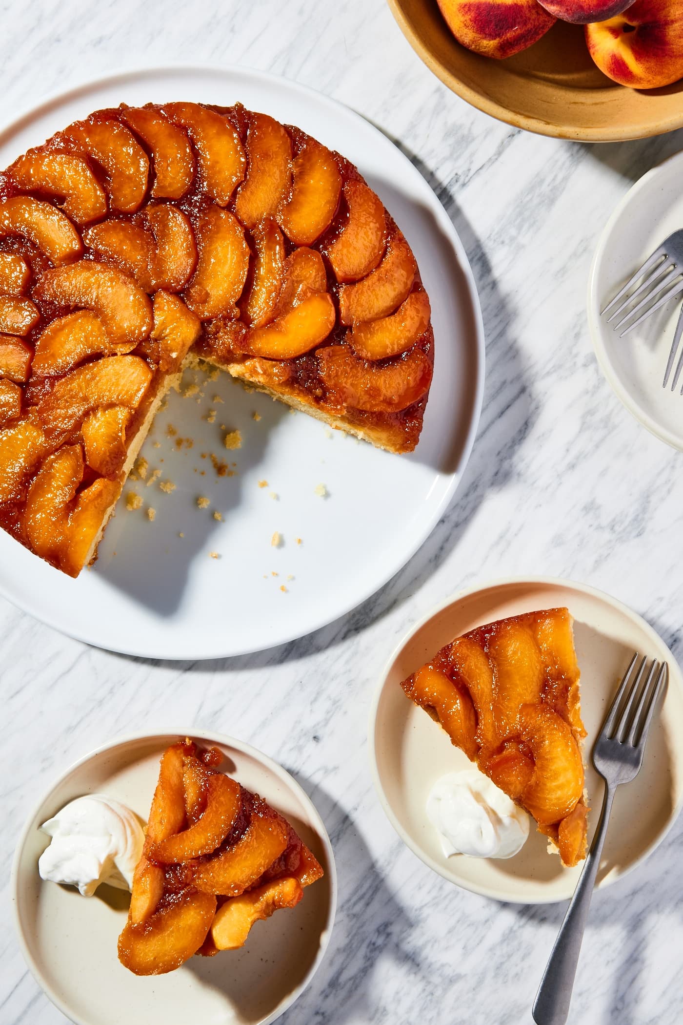 White marble surface with sliced upside down peach cake with two pieces sitting on taupe colored plates.