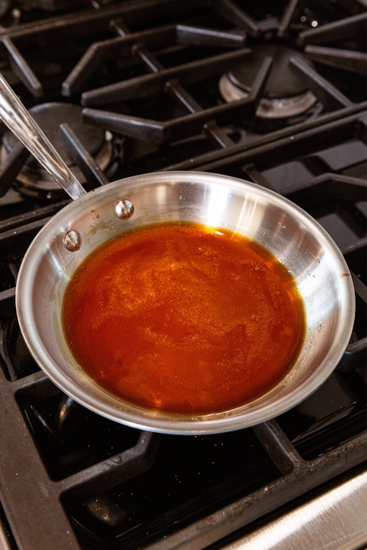 Metal skillet sitting on stovetop with melted sugar forming a caramel sauce in the pan.