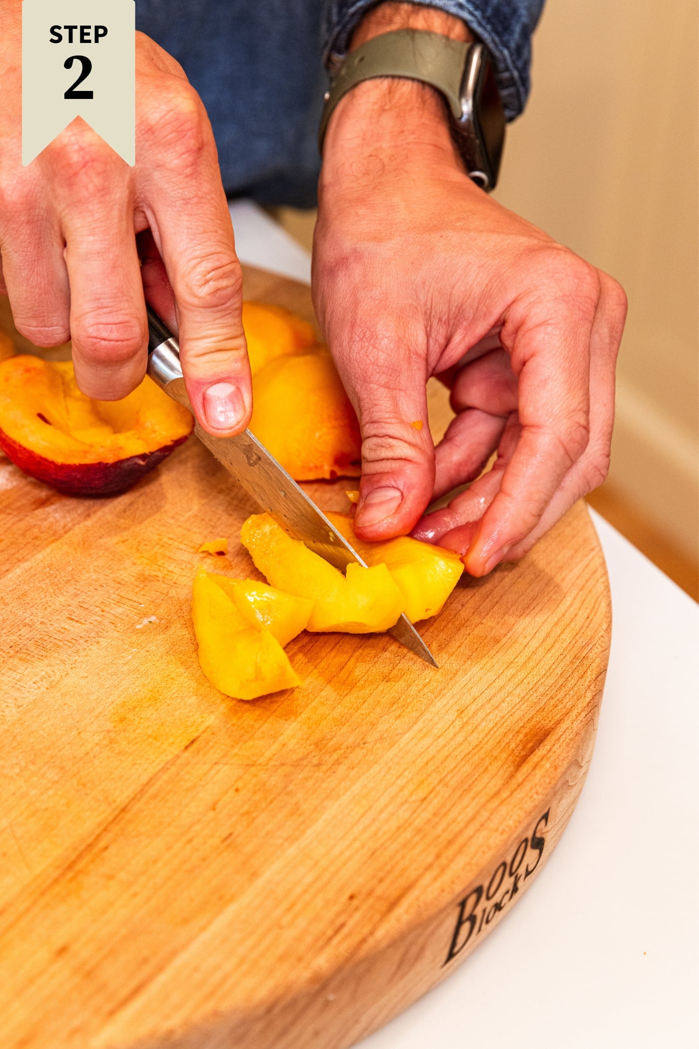 Hand using knife to slice peach into wedges on wood cutting board with more peaches behind.