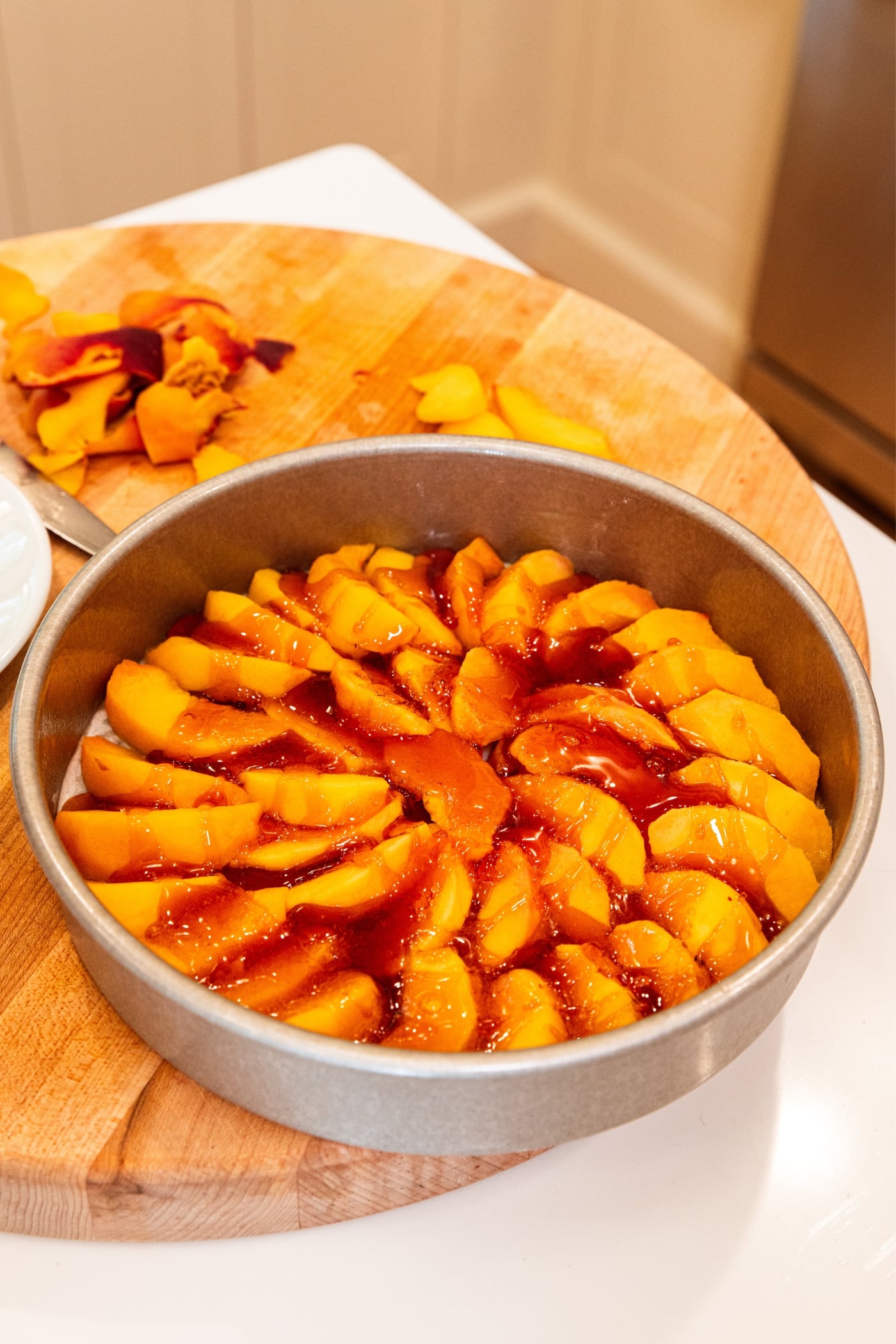 Melted caramel sauce resting on top of slices of peaches in round baking dish on wood cutting board.