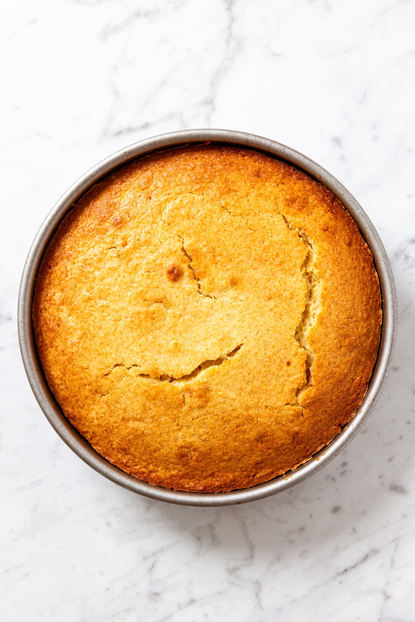Round metal baking pan sitting on white marble surface after being baked and coming out of the oven.