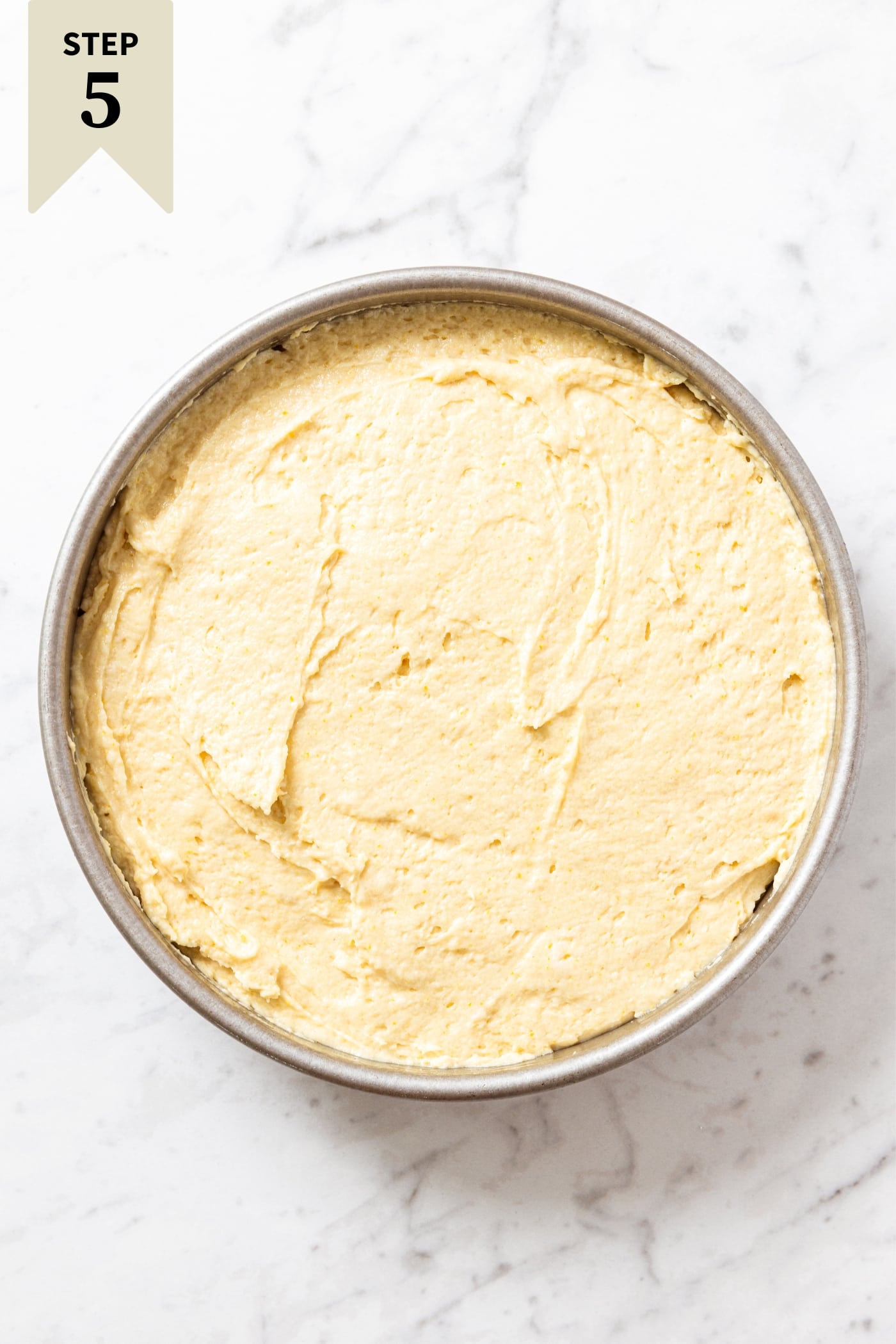 White marble surface with unbaked cake batter in round metal baking pan.