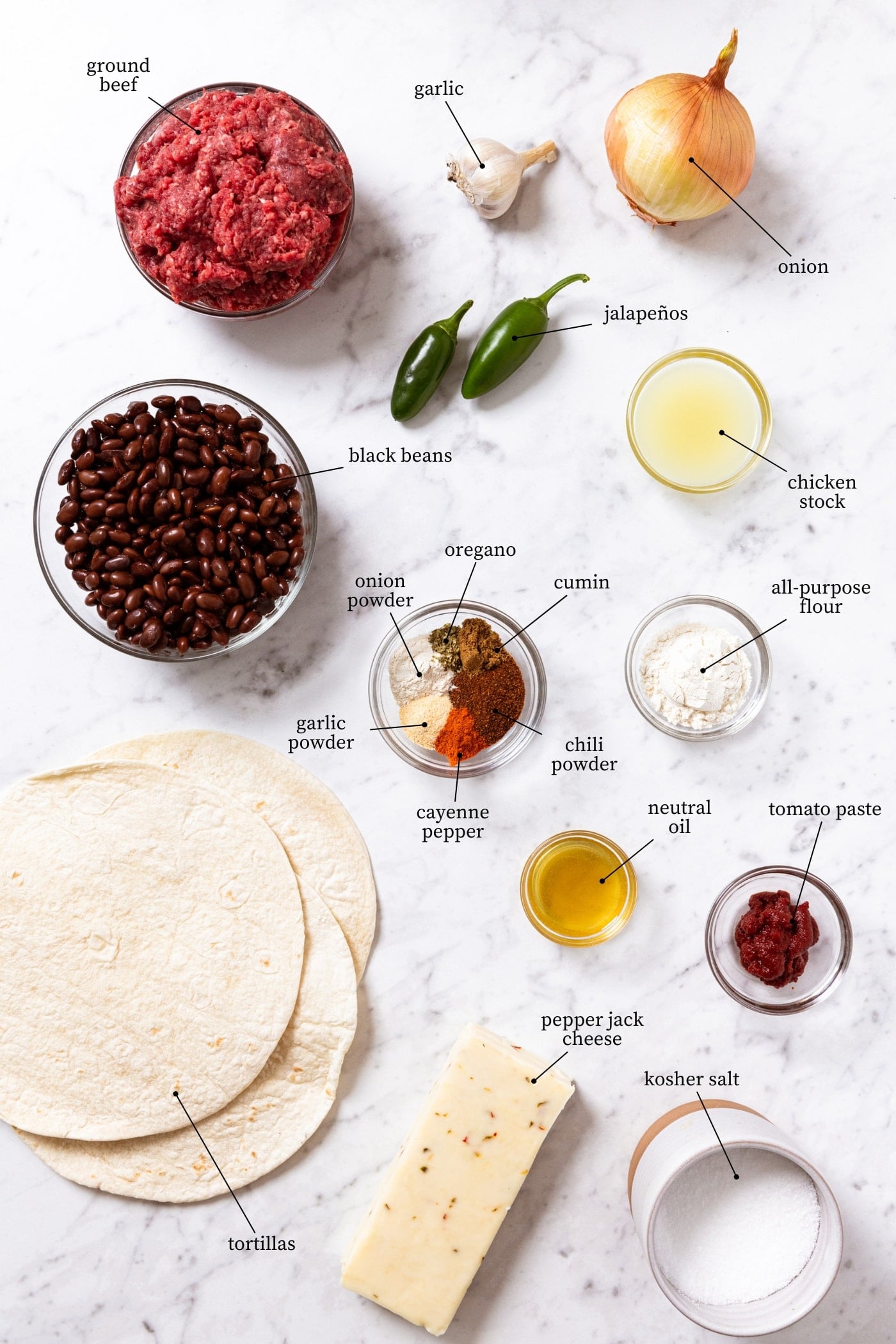 White marble surface filled with all ingredients needed to make beef enchiladas including beef, beans, tortillas, cheese, spices, and more.