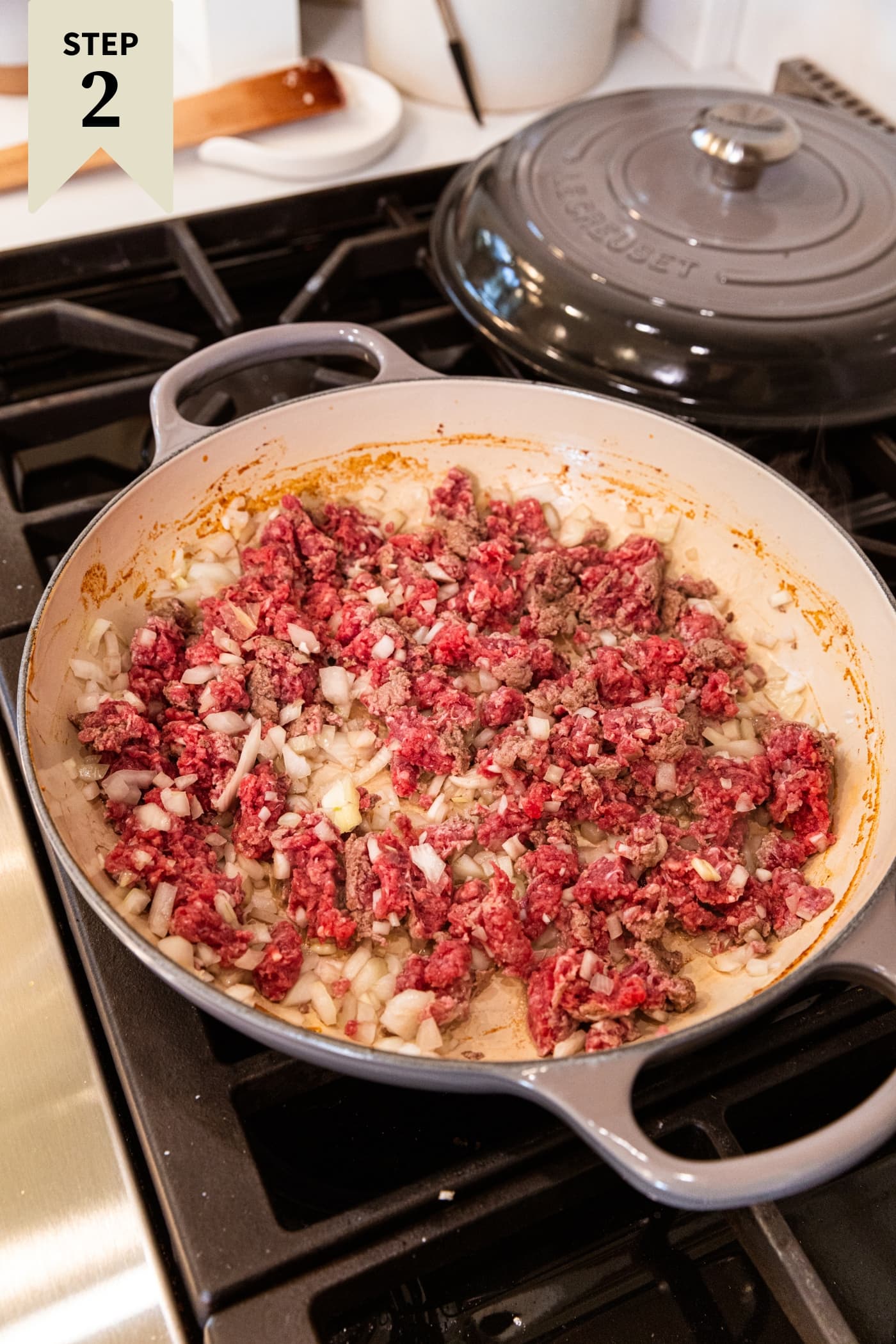 Raw meat and onion mixture sitting in a pot on the stove before being mixed together and browned.