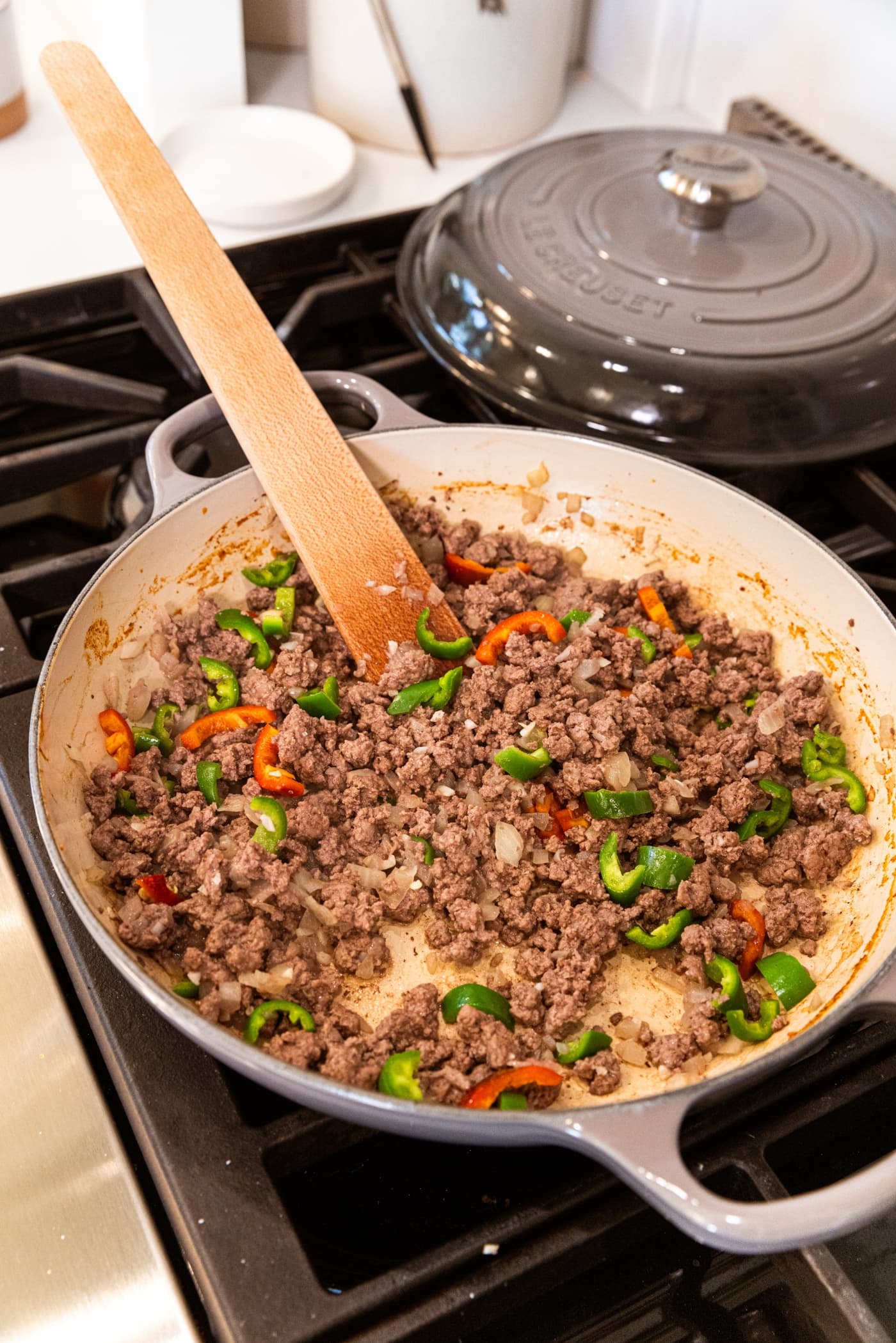 Large pan filled with cooked browned meat with jalapeños with wooden spatula resting against the back of the pan.