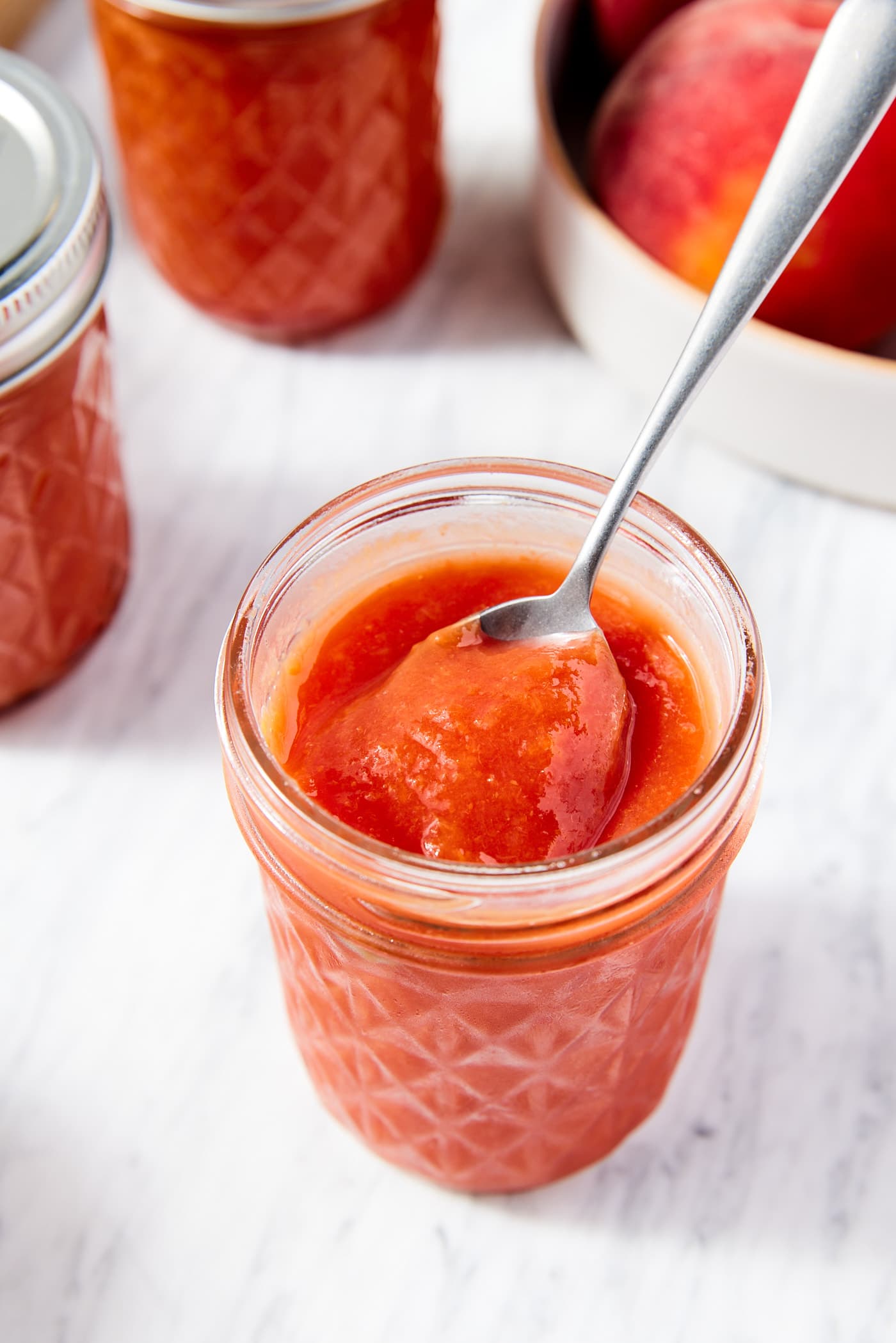 Jam jar filled with orange-colored peach butter with spoon resting on jar about to scoop out a serving.