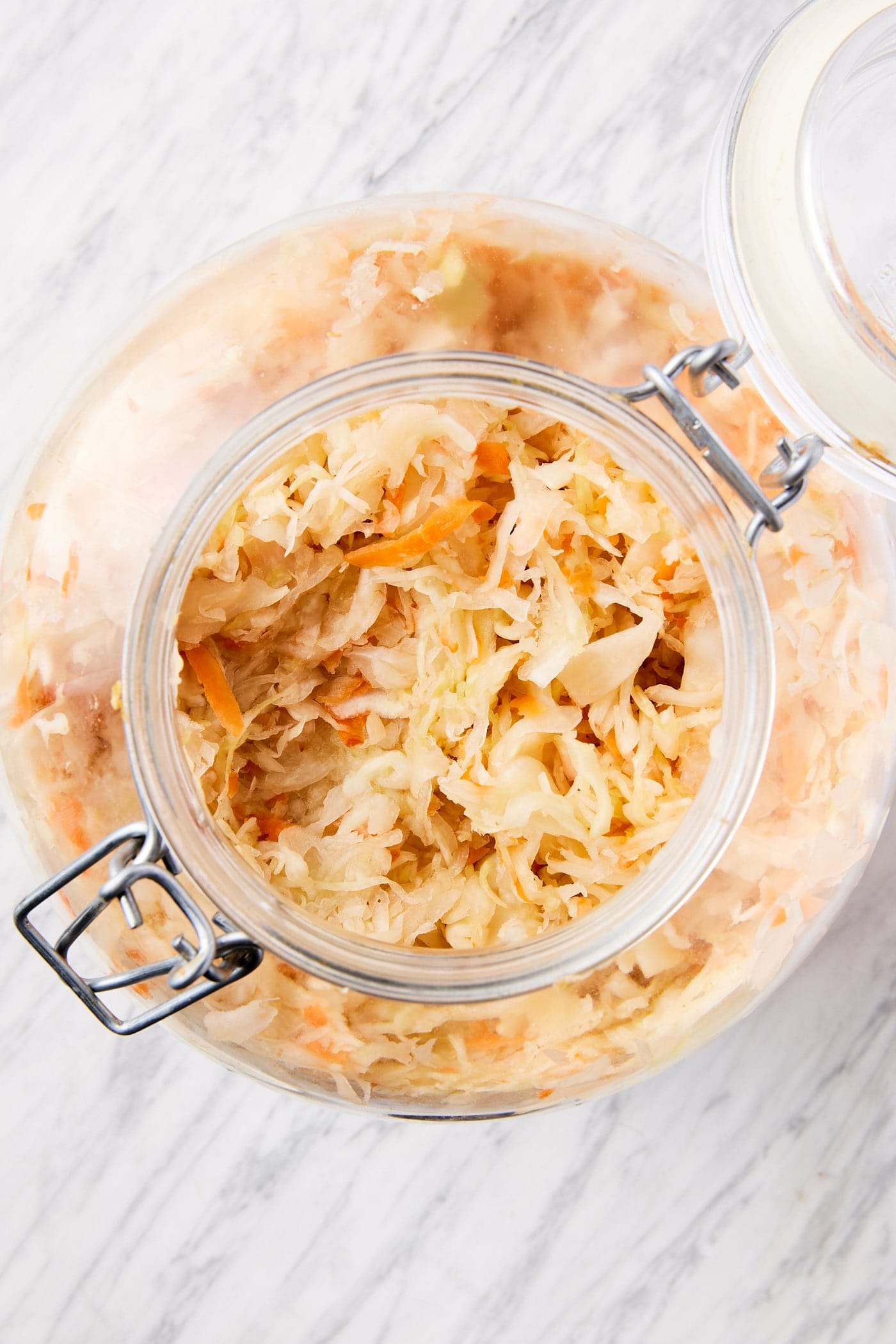 Big glass jar filled with homemade sauerkraut with pieces of carrot included in the mixture along with the shredded cabbage.
