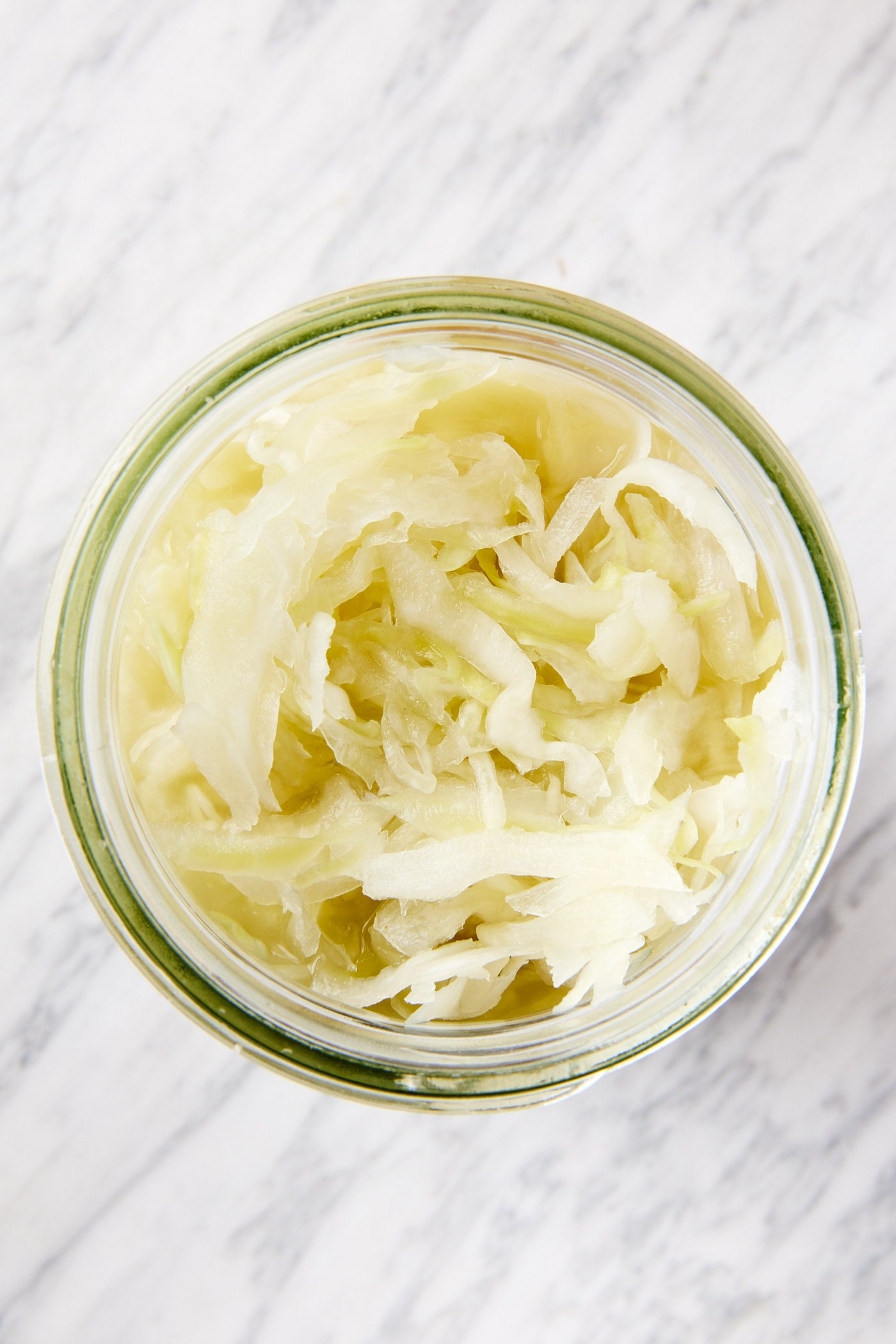 White marble surface with glass quart jar filled with homemade sauerkraut showing texture of finished recipe.