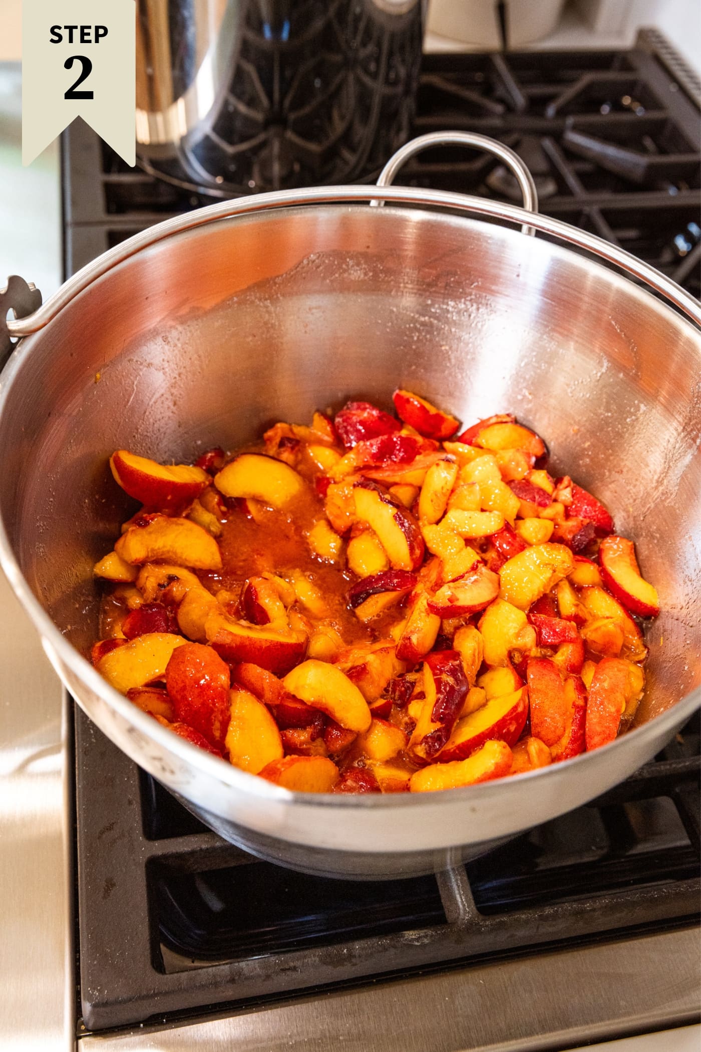 Large metal stockpot filled with sliced peaches sitting on stovetop before being cooked down with the heat.