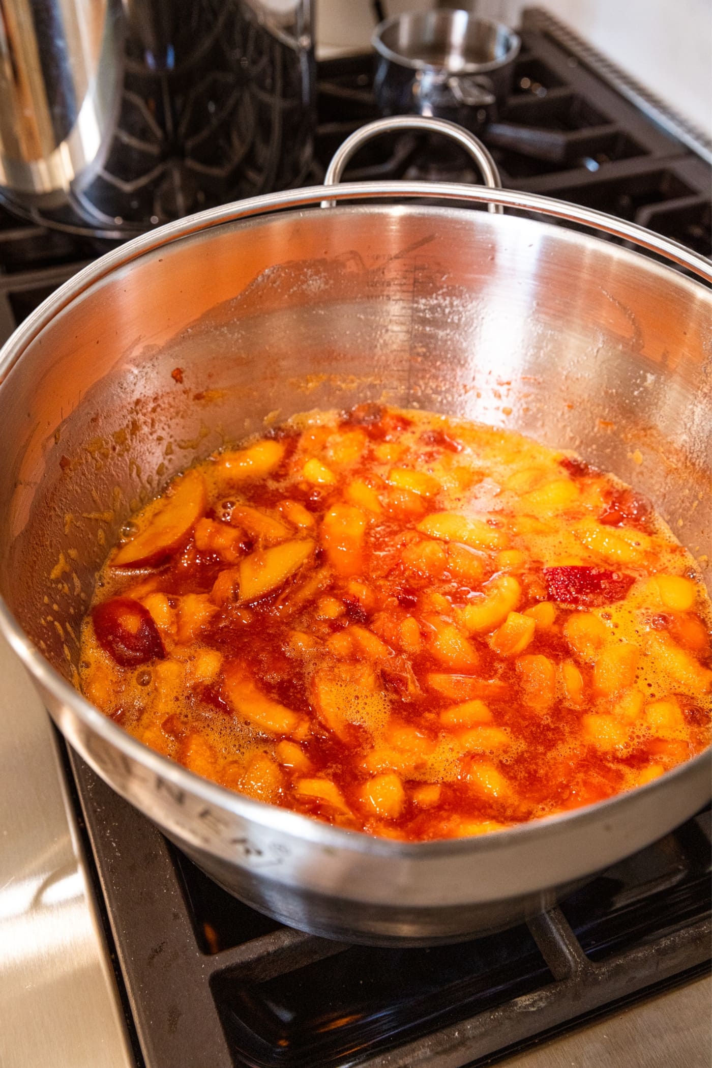Large metal stockpot sitting on stovetop with sliced peaches cooking in their own juices.