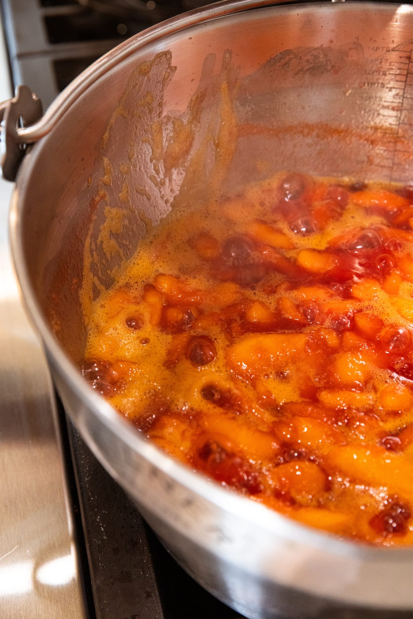 Large metal stockpot sitting on stovetop with juices bubbling from sliced peaches cooking down in their own juices.
