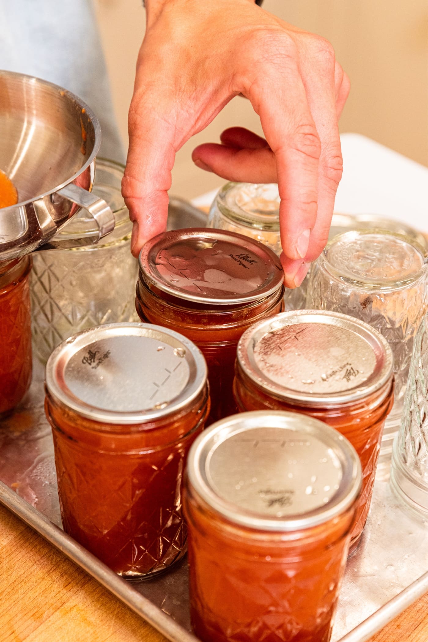 Hand placing metal lid on jam jar filled with peach butter.