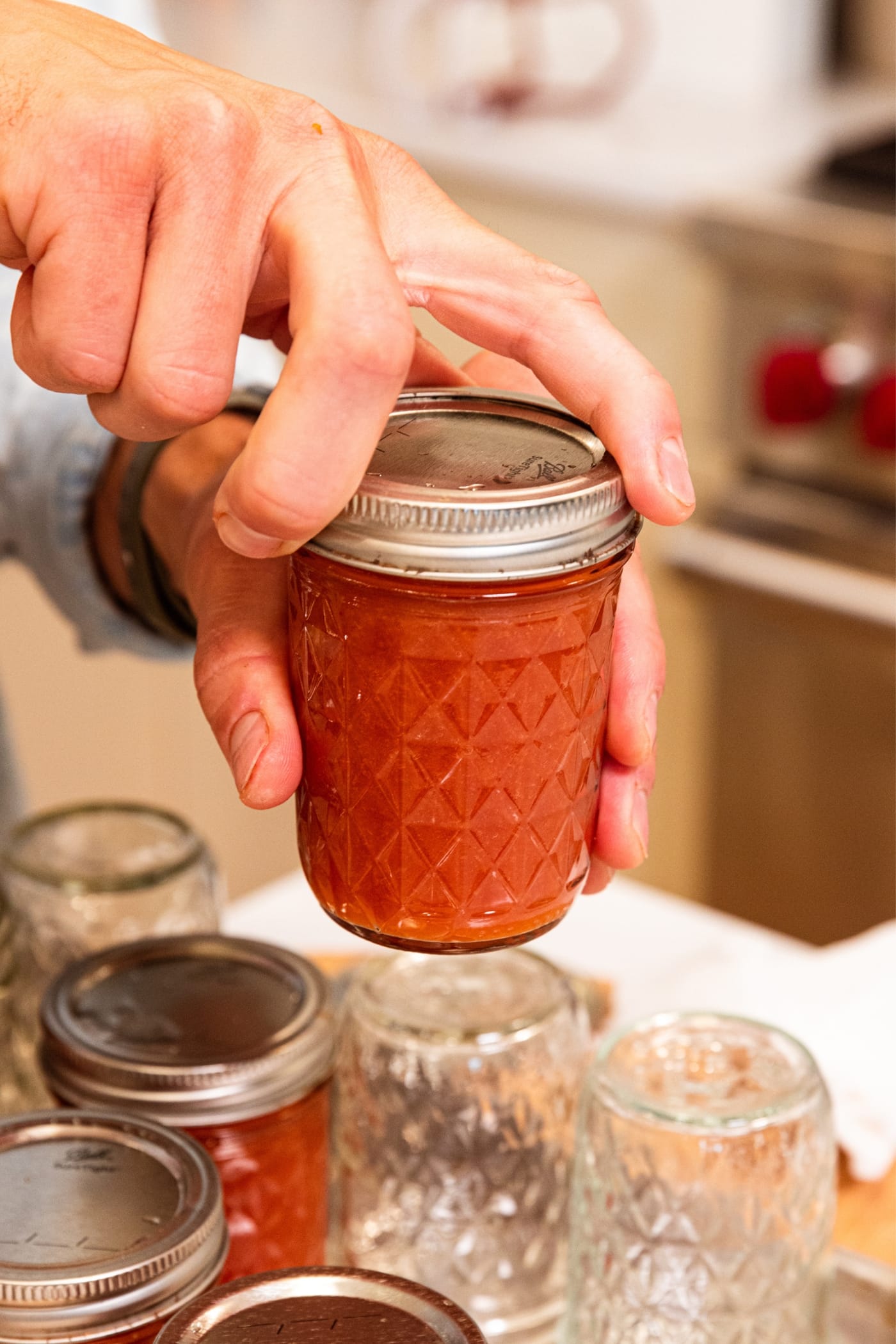 Hand screwing lid on top of jam jar filled with peach butter with rest of jam jars below.