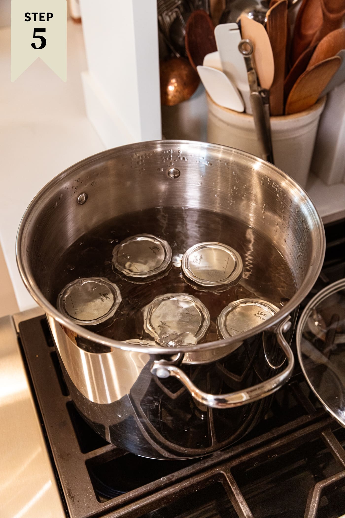 Large stockpot sitting on stovetop with water bath inside with jam jars with lids and rings on top.