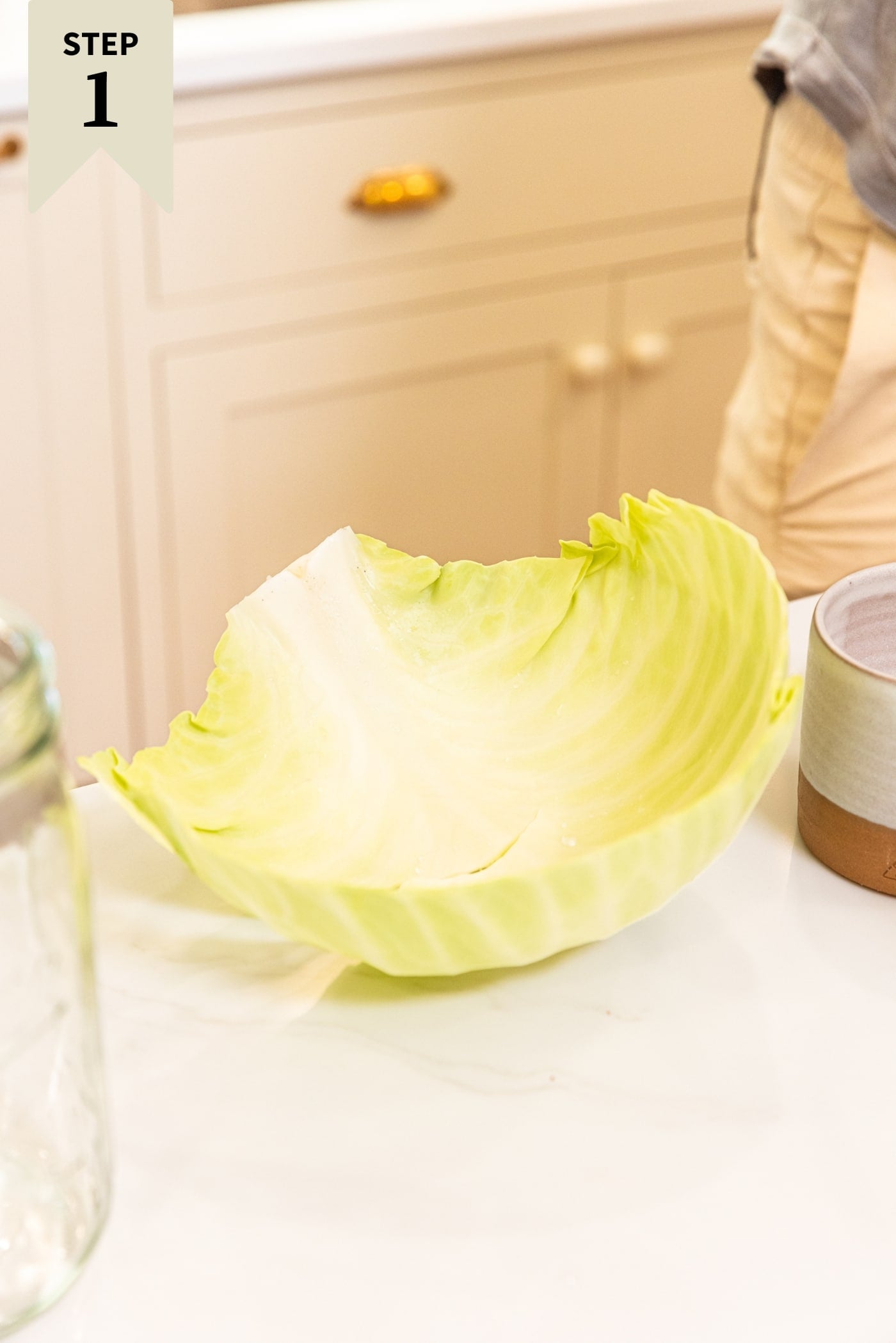 Outer piece of big head of cabbage resting on white countertop in a kitchen with salt cellar right beside.