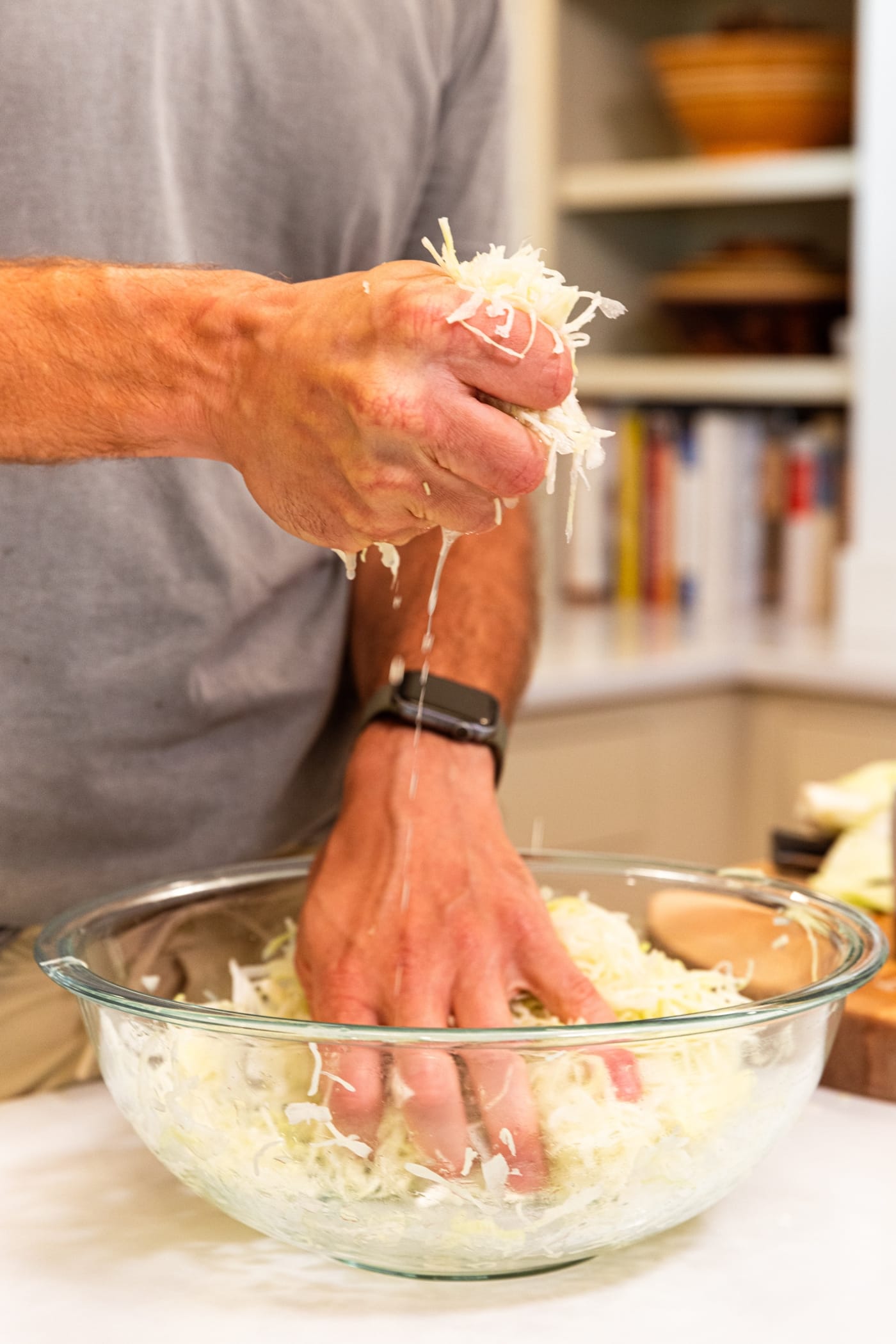 Hand holding fistful of shredded cabbage squishing it to release some of the juice into a large glass bowl underneath.