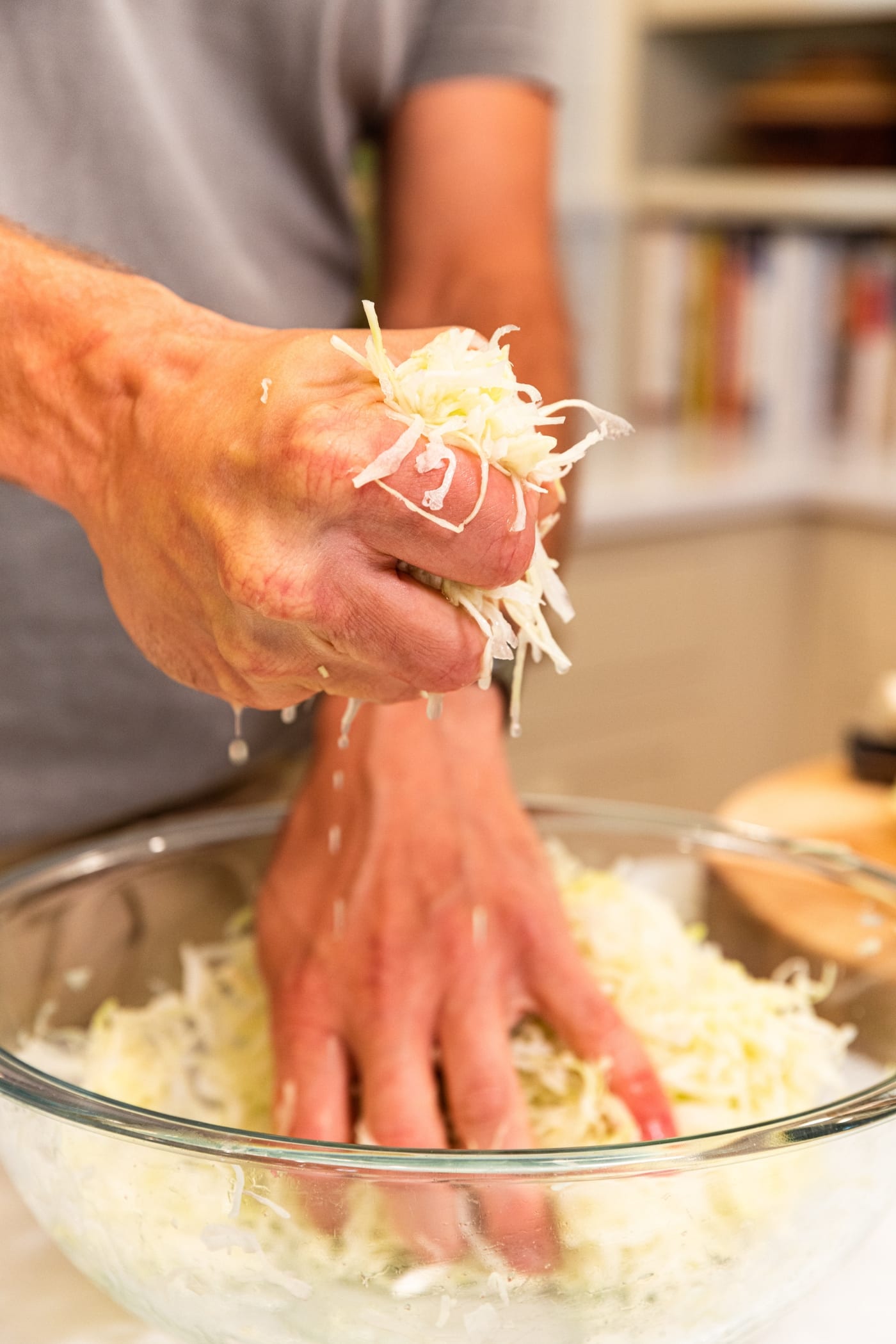 Hand holding fistful of shredded cabbage with liquid dripping out of fist from the cabbage.