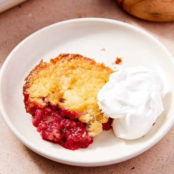 White plate with serving of raspberry cobbler sitting on plate with dollop of whipped cream.