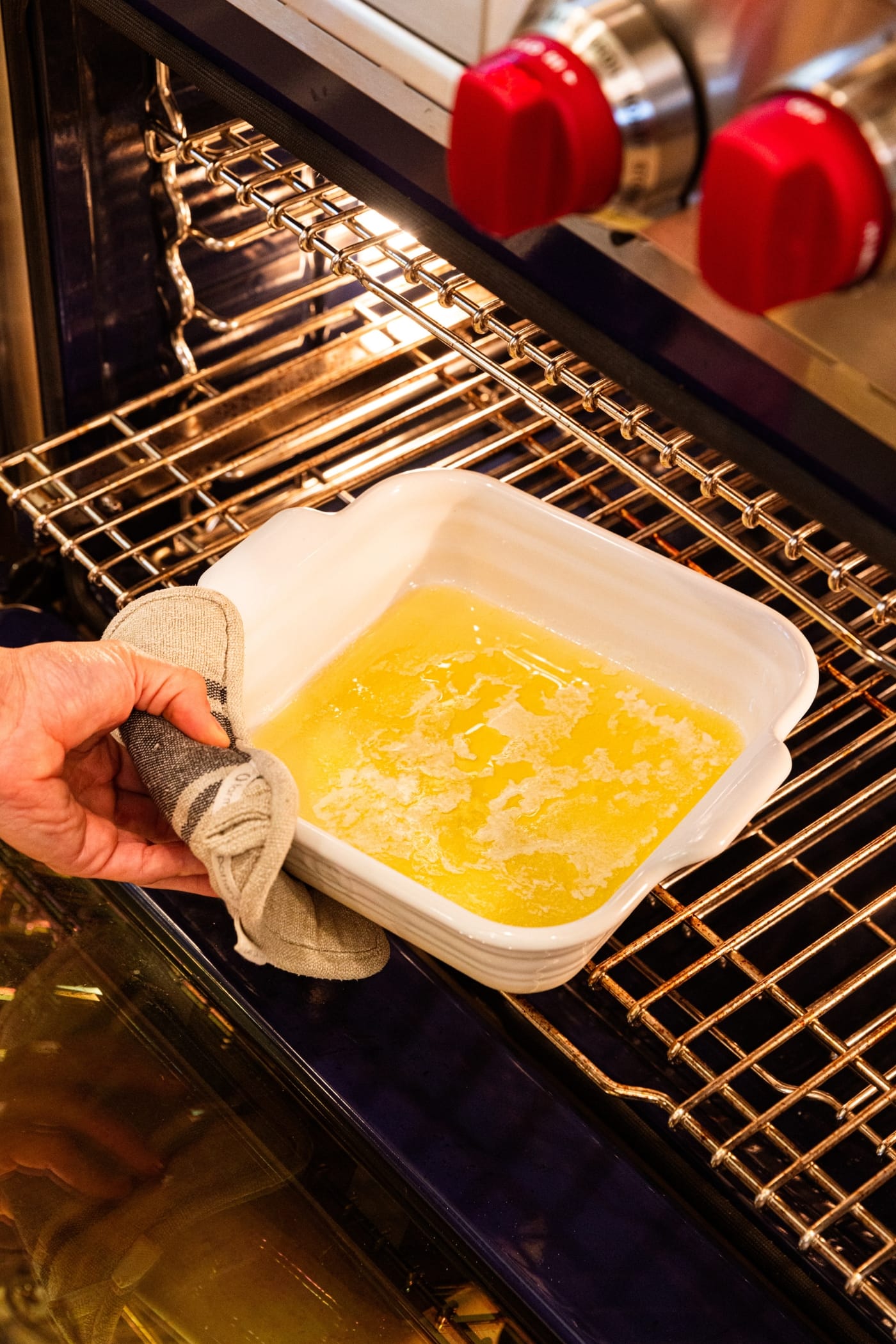 Hand holding hot pad pulling a baking pan from the oven containing melted butter.