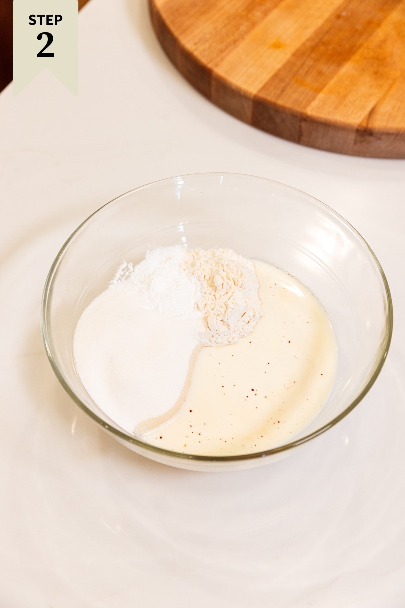 Glass bowl filled with ingredients needed for a cobbler batter including flour and milk all on white surface.