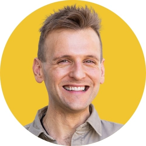 Kaleb Wyse wearing brown shirt standing in front of bright yellow background smiling.