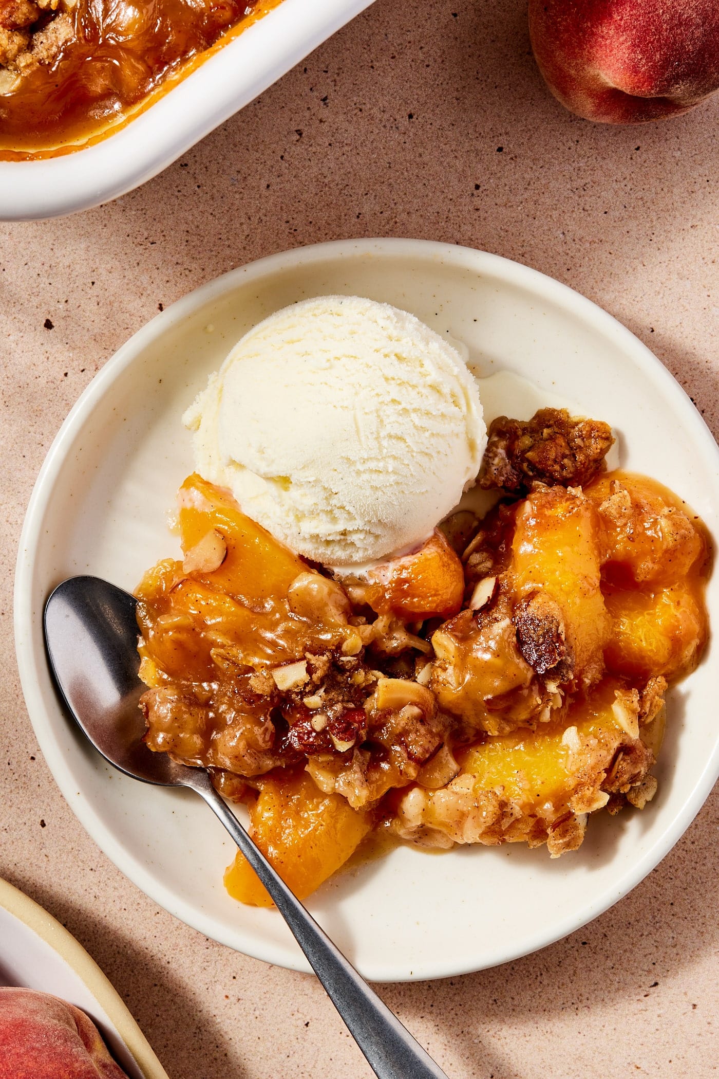 Large white plate filled with scoop of peach crisp with scoop of ice cream on top along with spoon.