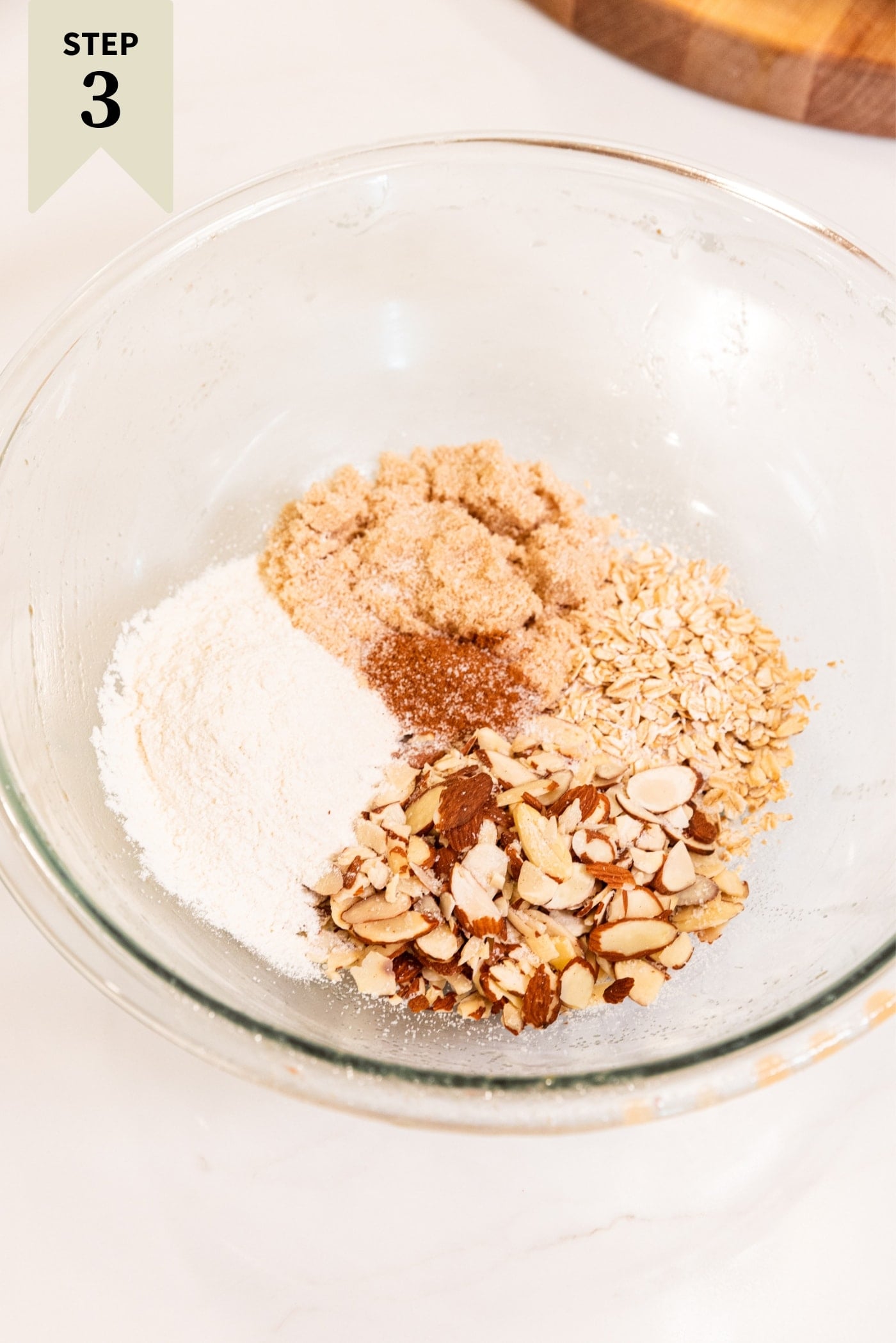 Glass mixing bowl filled with streusel ingredients including flour, almonds, sugar, spices, and more before mixing everything together.