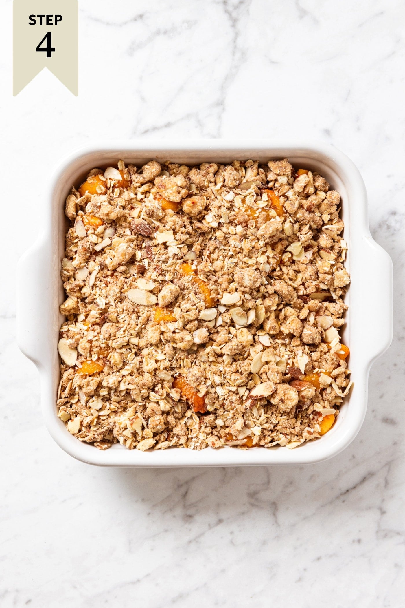 White marble surface with unbaked peach crisp with streusel topping sprinkled all over the top right before going into the oven.